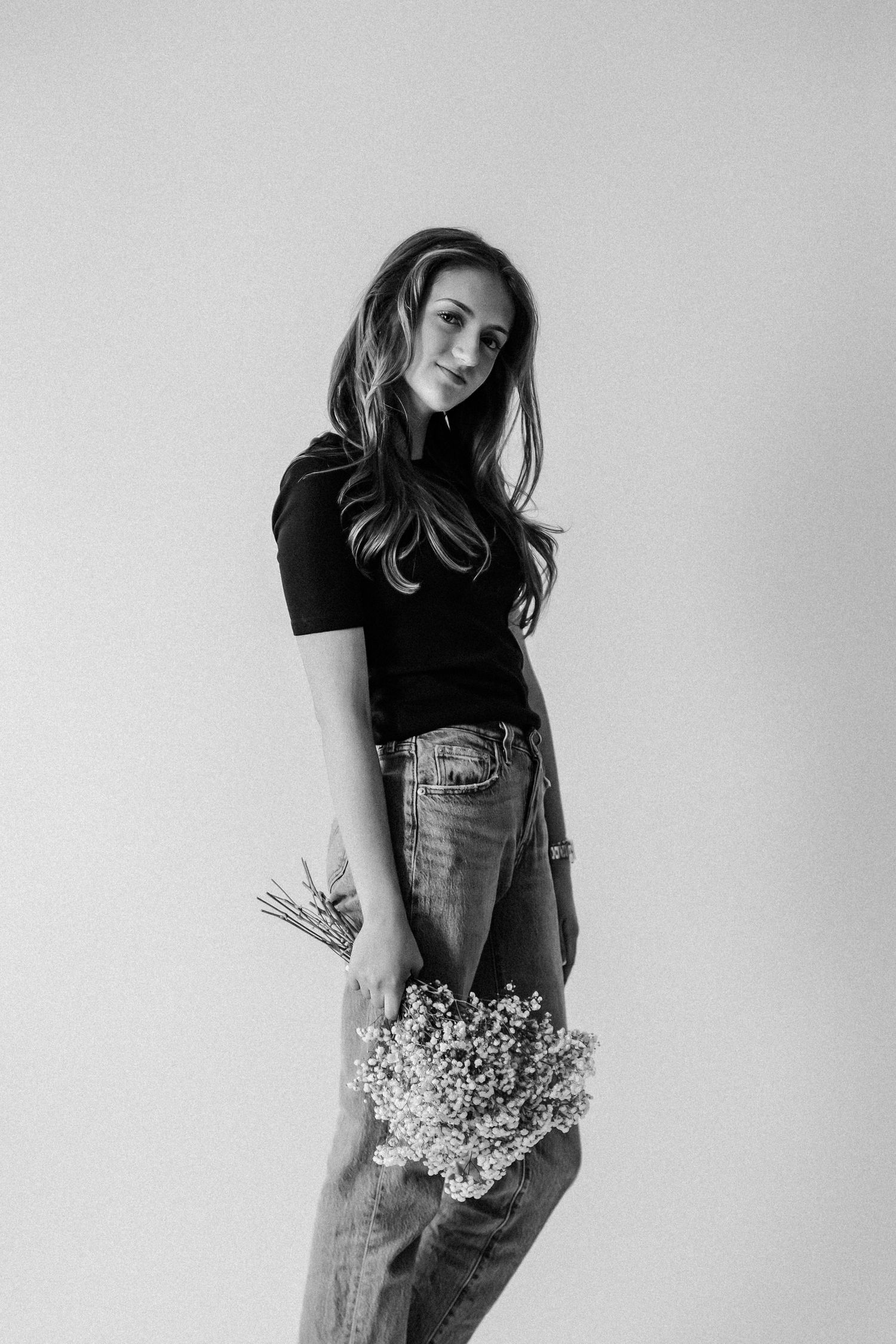 Woman in black t-shirt and jeans holds bouquet of white flowers in black and white studio portrait.