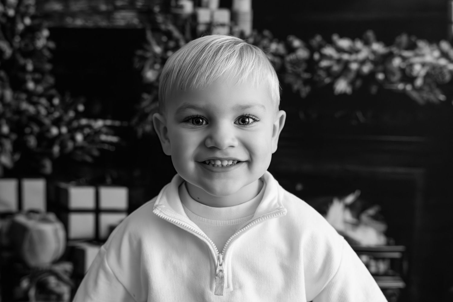 Black and white portrait of a child in a white shirt against a dark background.