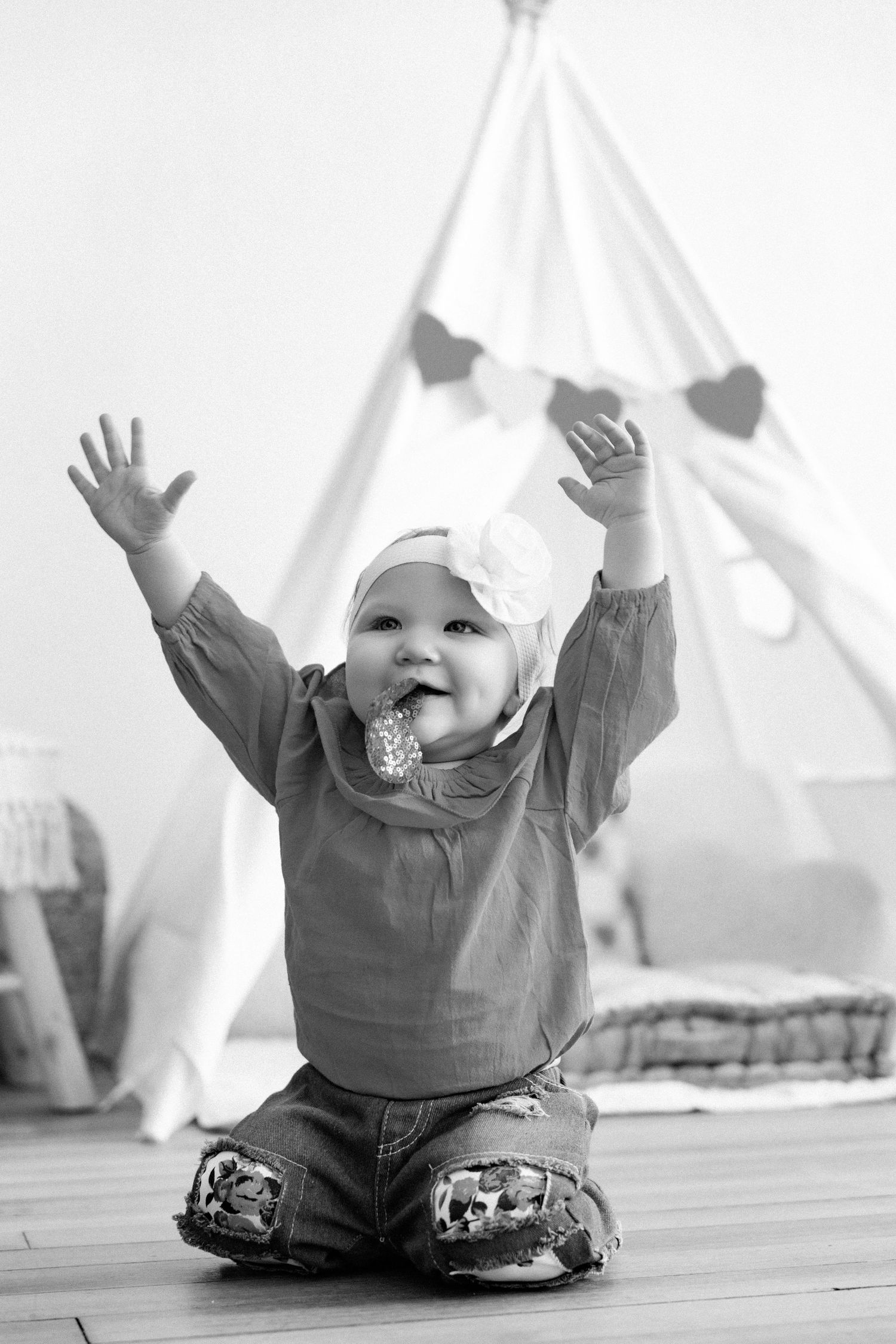Black and white photos of baby playing and raising arms near white tent.