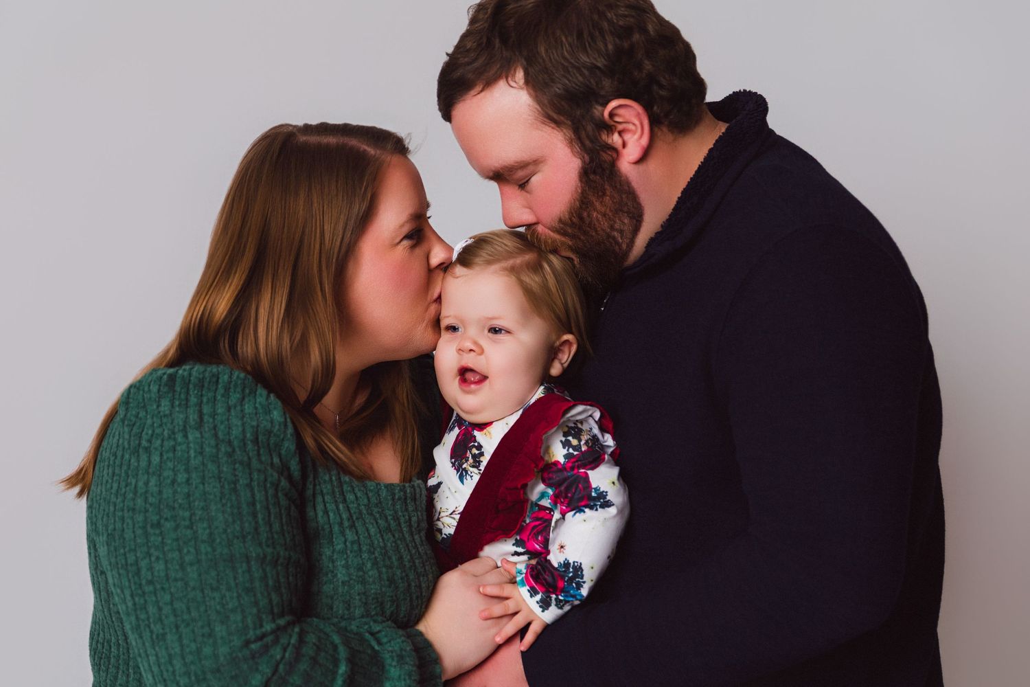 Intimate family portrait against gray background showing warm embrace and joyful expressions.