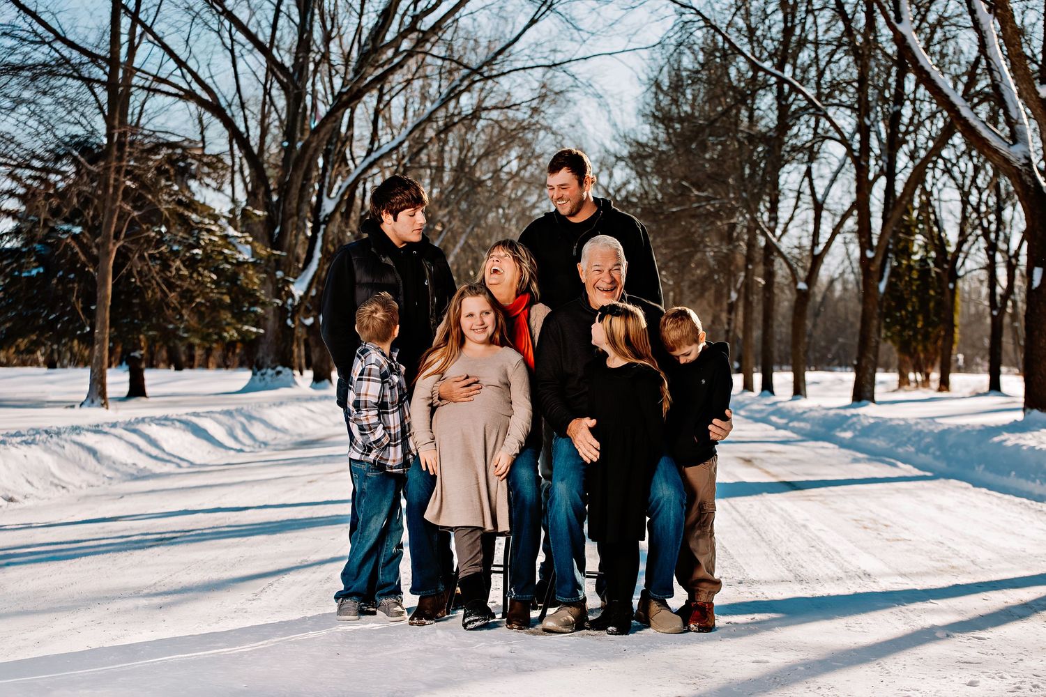 A family group poses together on a snowy winter path with bare trees in the background.
