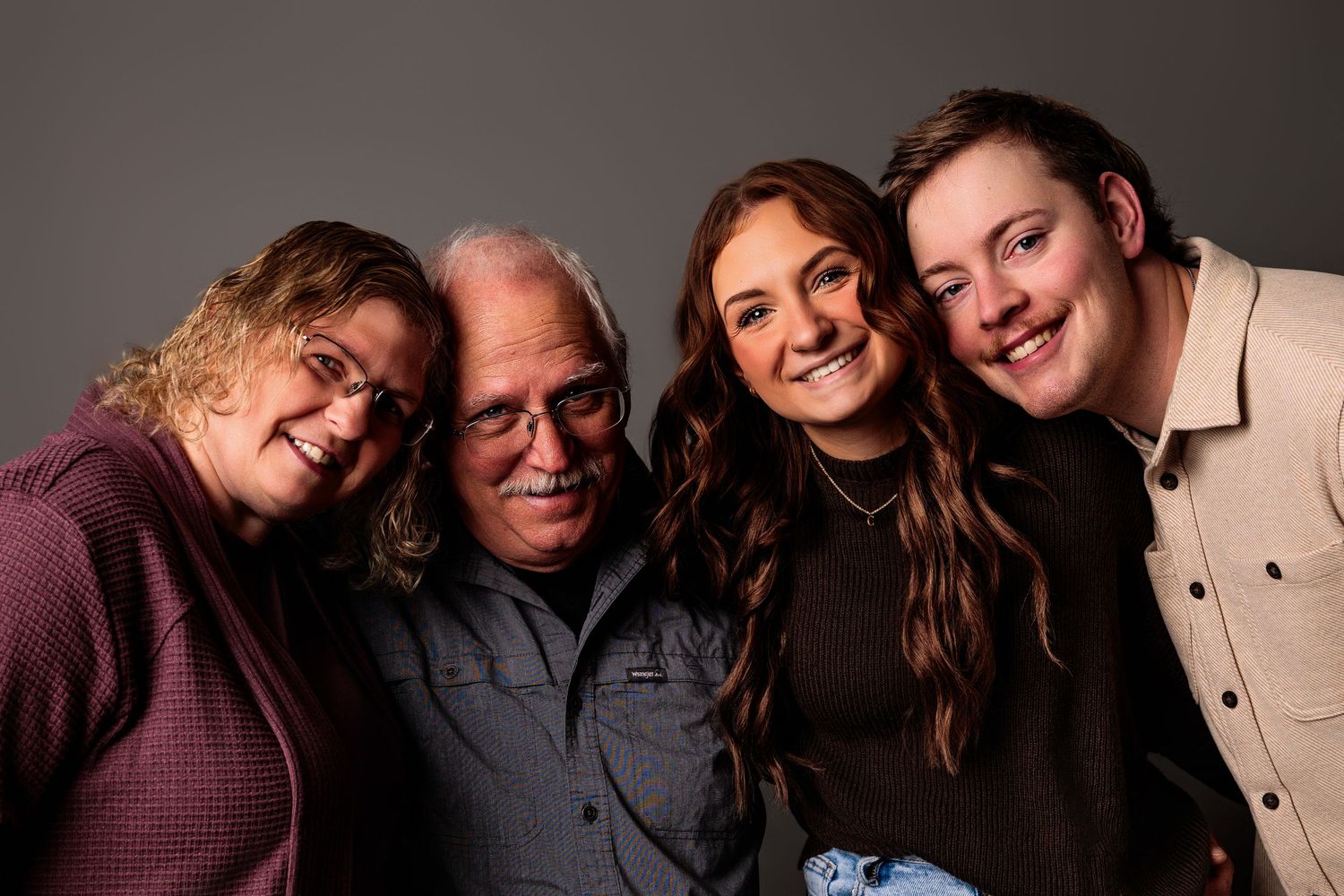 Four smiling family members pose together for a professional portrait against a gray studio background.