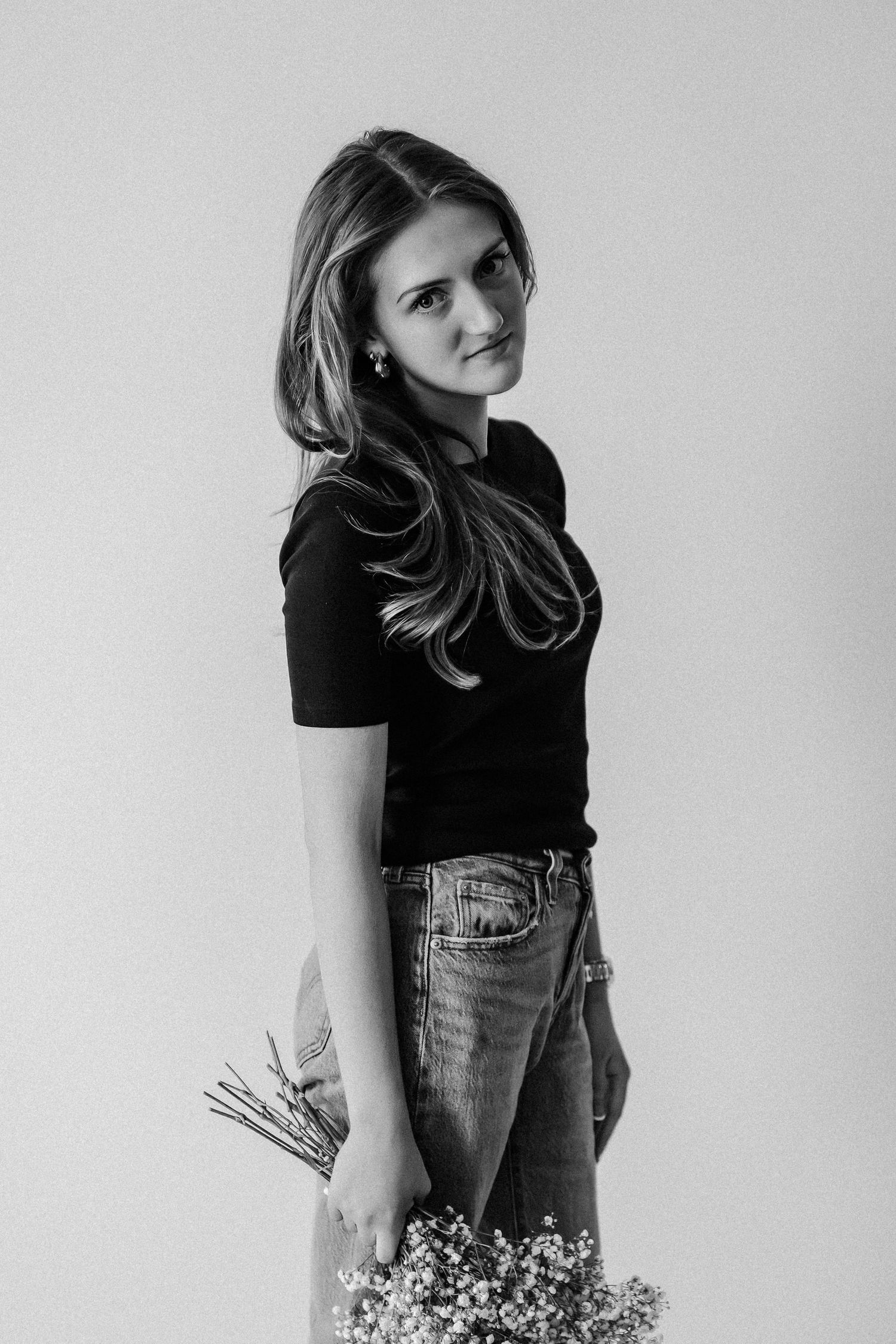 Black and white portrait of young woman in black tee and jeans holding wildflowers, side profile.