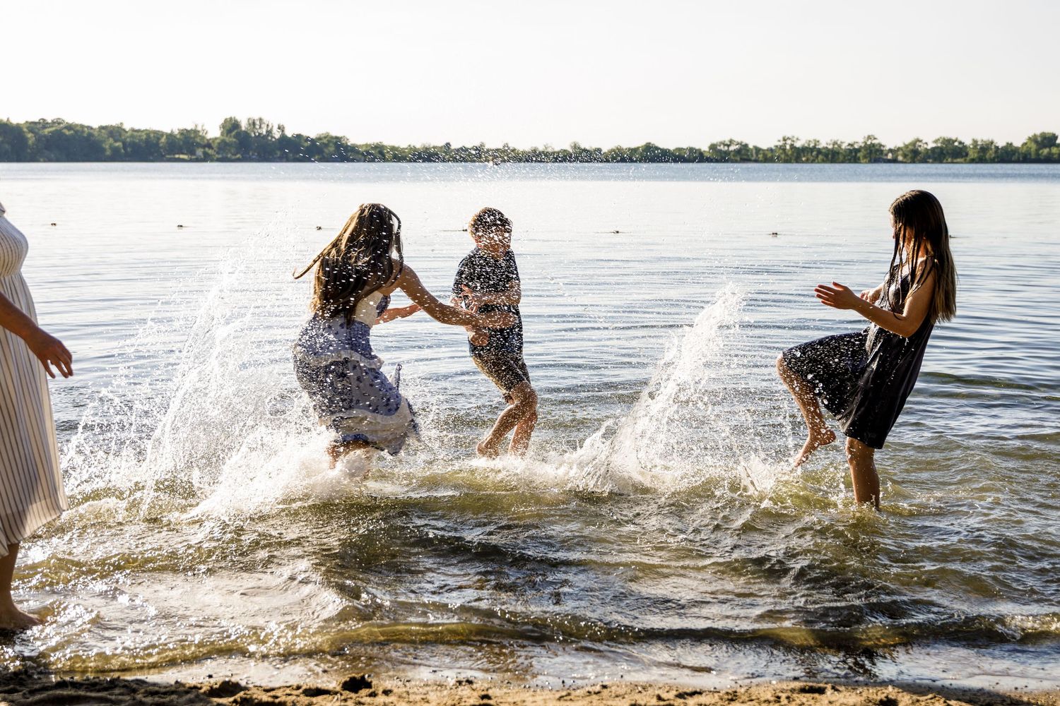 Group of people laughing and splashing each other in a shallow lake on a sunny day.