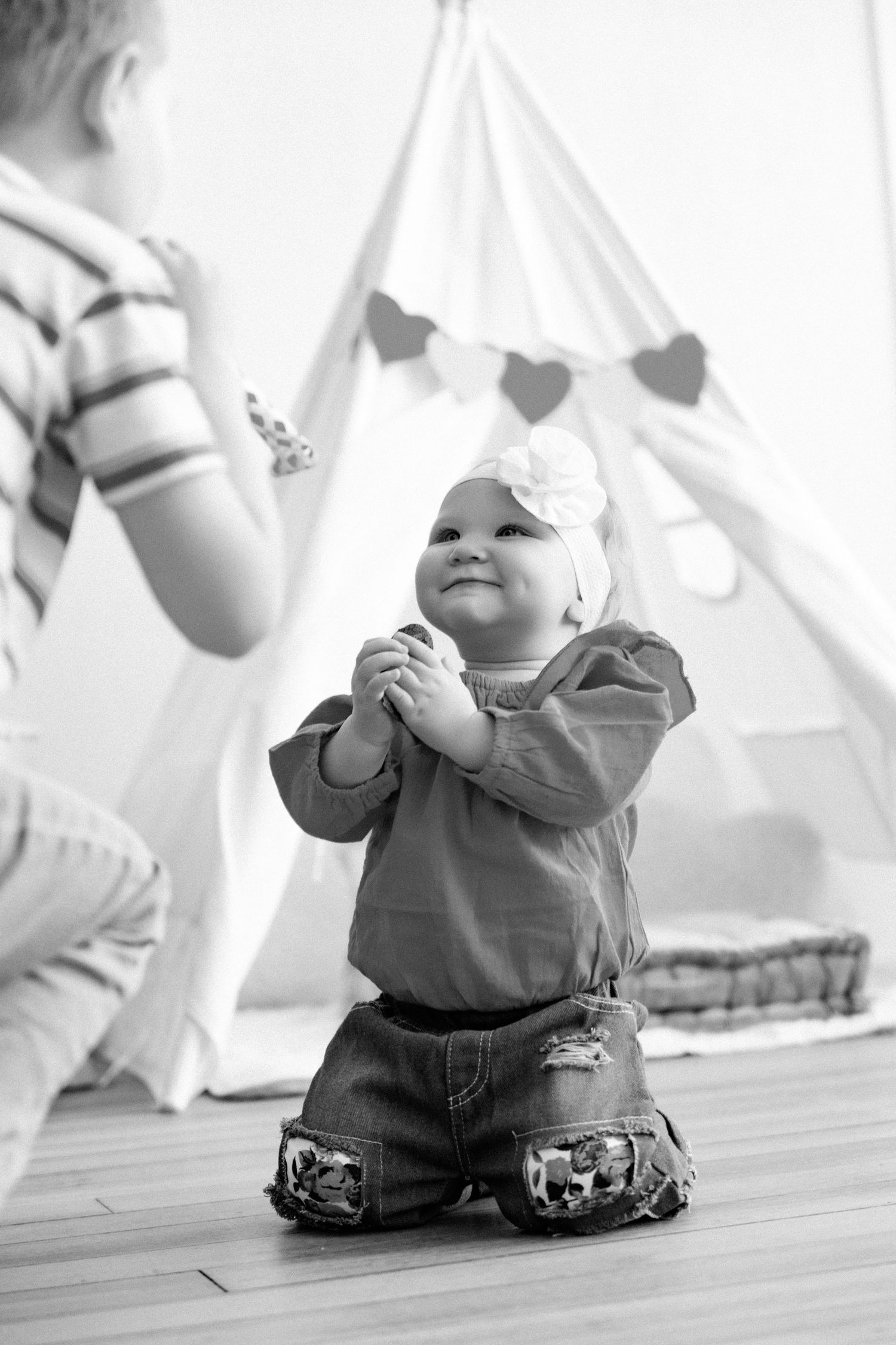 Black and white series of candid moments on wooden floor with teepee and heart garland.