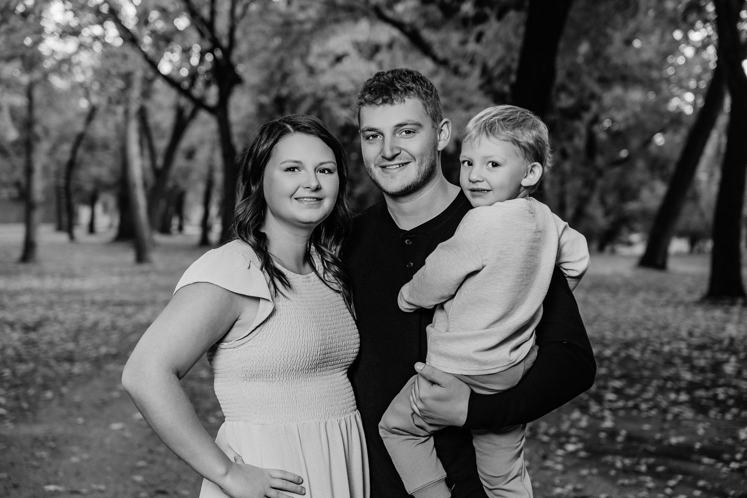 A family embraces while standing in a wooded park during autumn.