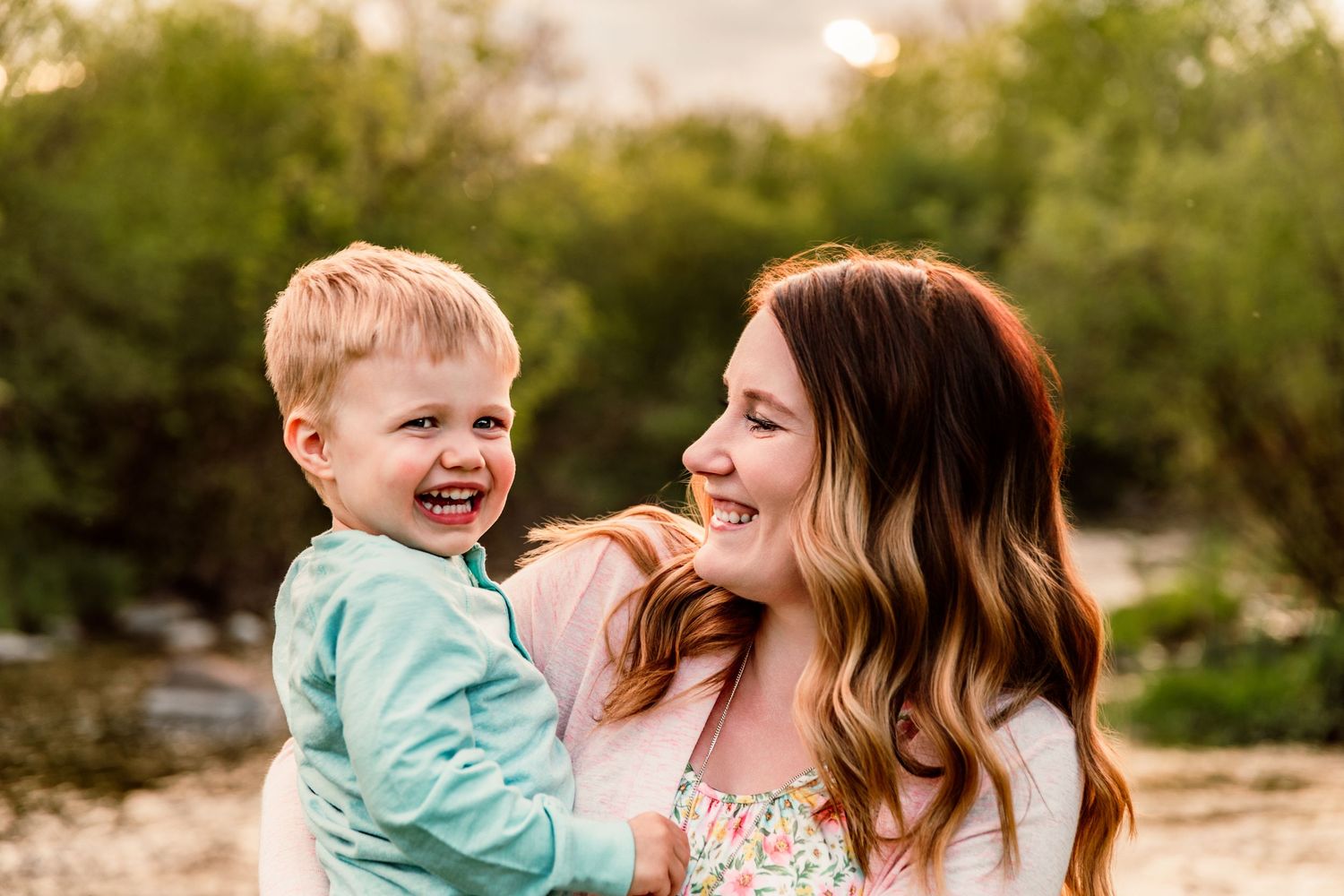 A joyful mother and toddler boy laughing together outdoors in warm golden light.