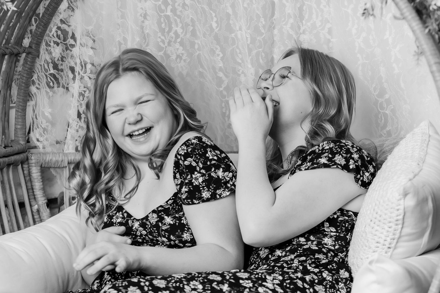 Two sisters laughing together in black and white photo seated in a wicker chair.