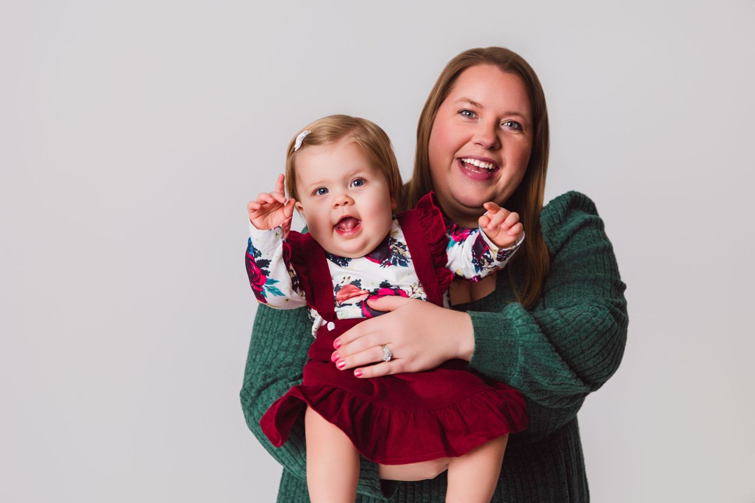 Mother and baby in festive holiday outfits share joyful laughter against white background.