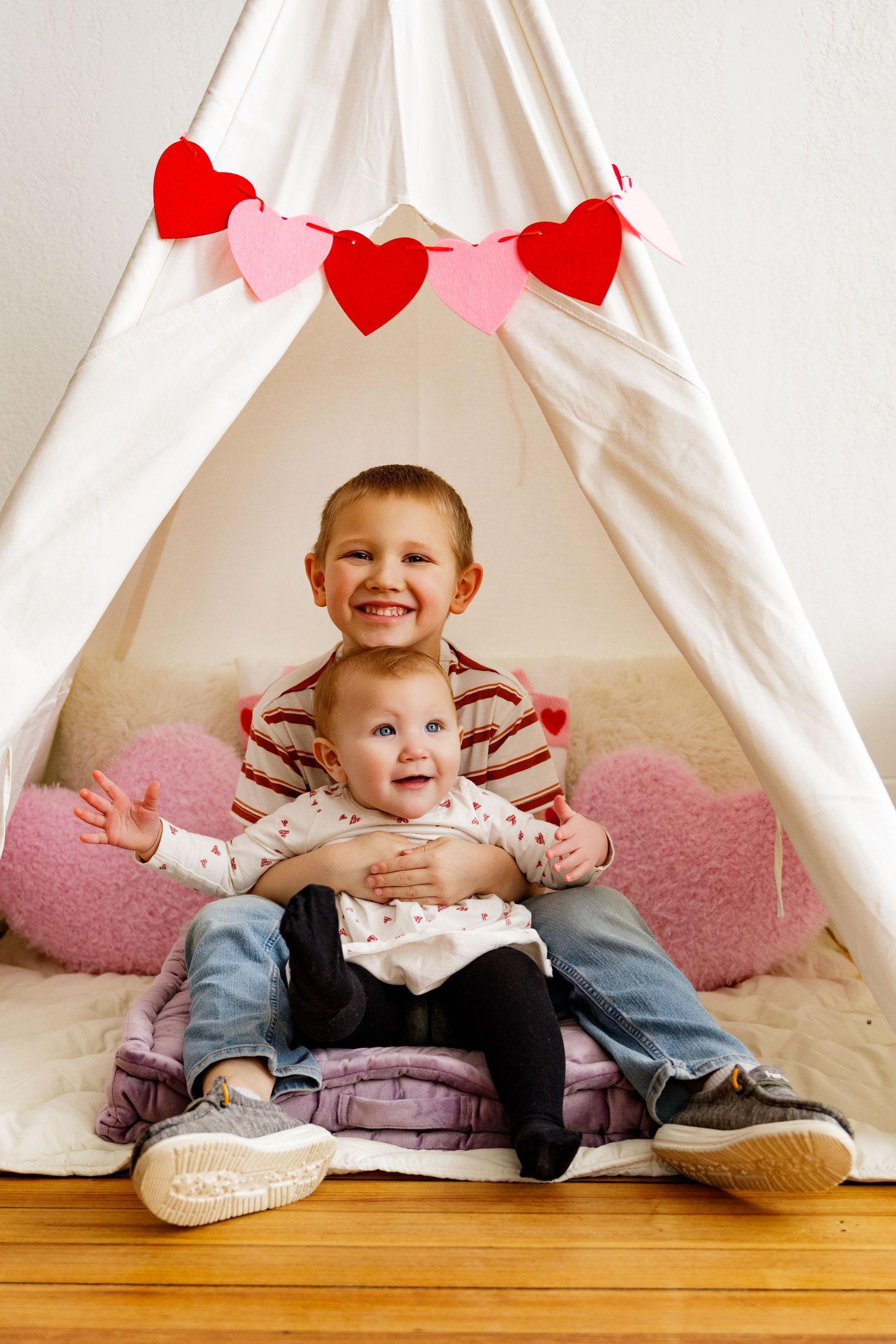Sweet Valentine's day photo setup with a white tent, pink heart rug, and red heart banner decorations.