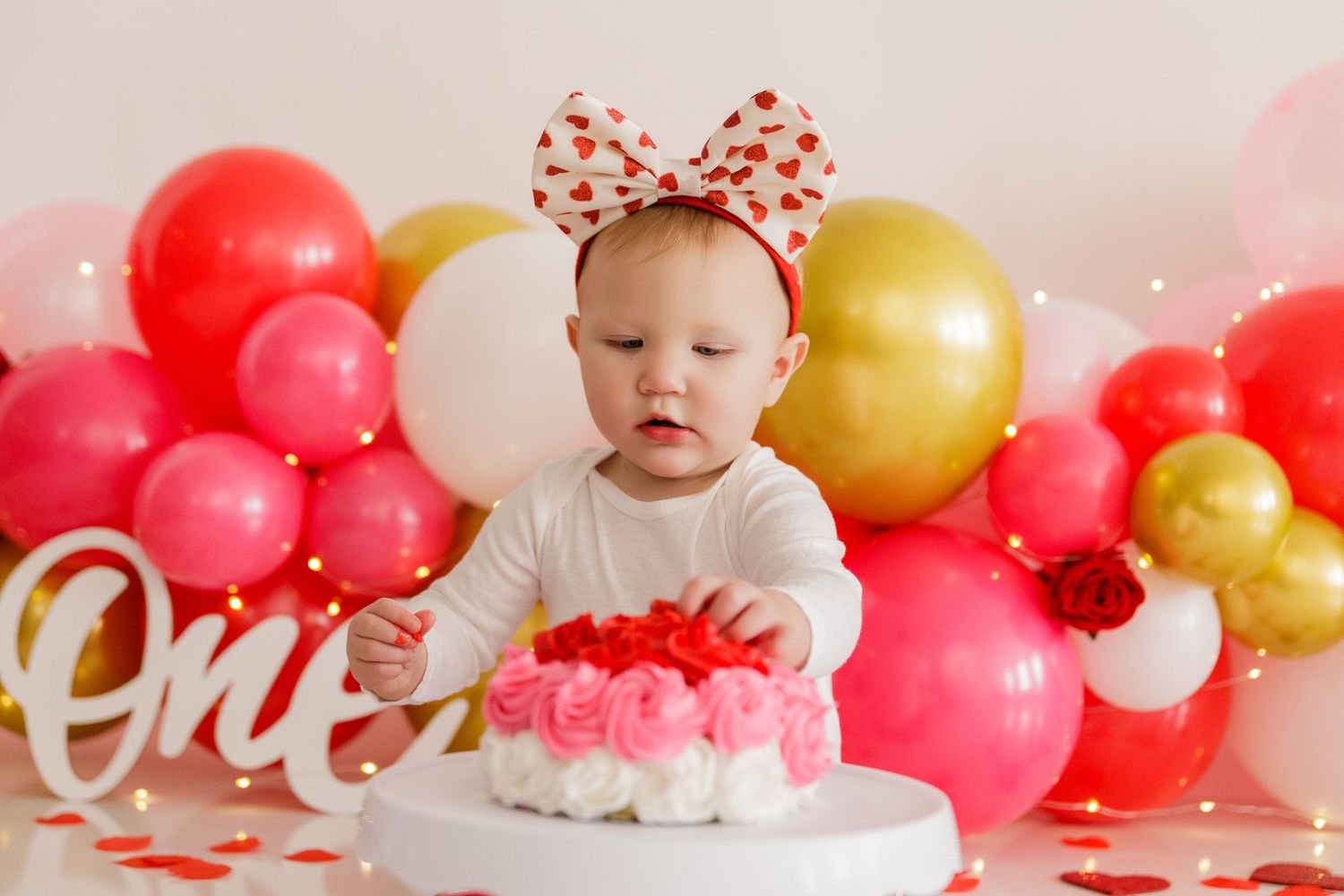 First birthday cake smash setup with pink and gold balloon garland and white cake stand.