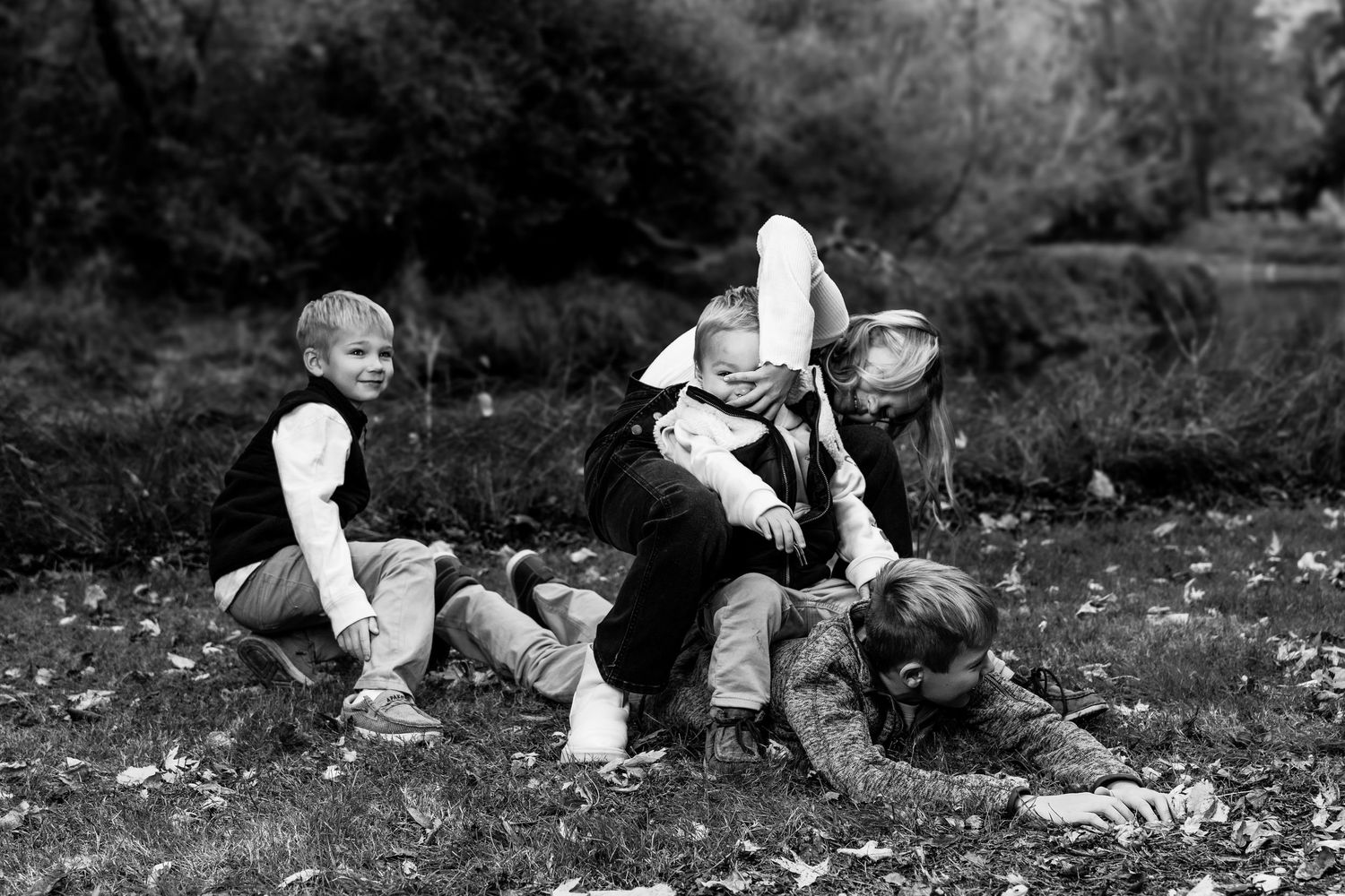 Black and white series showing playful couple lying in fallen leaves during outdoor photo session.