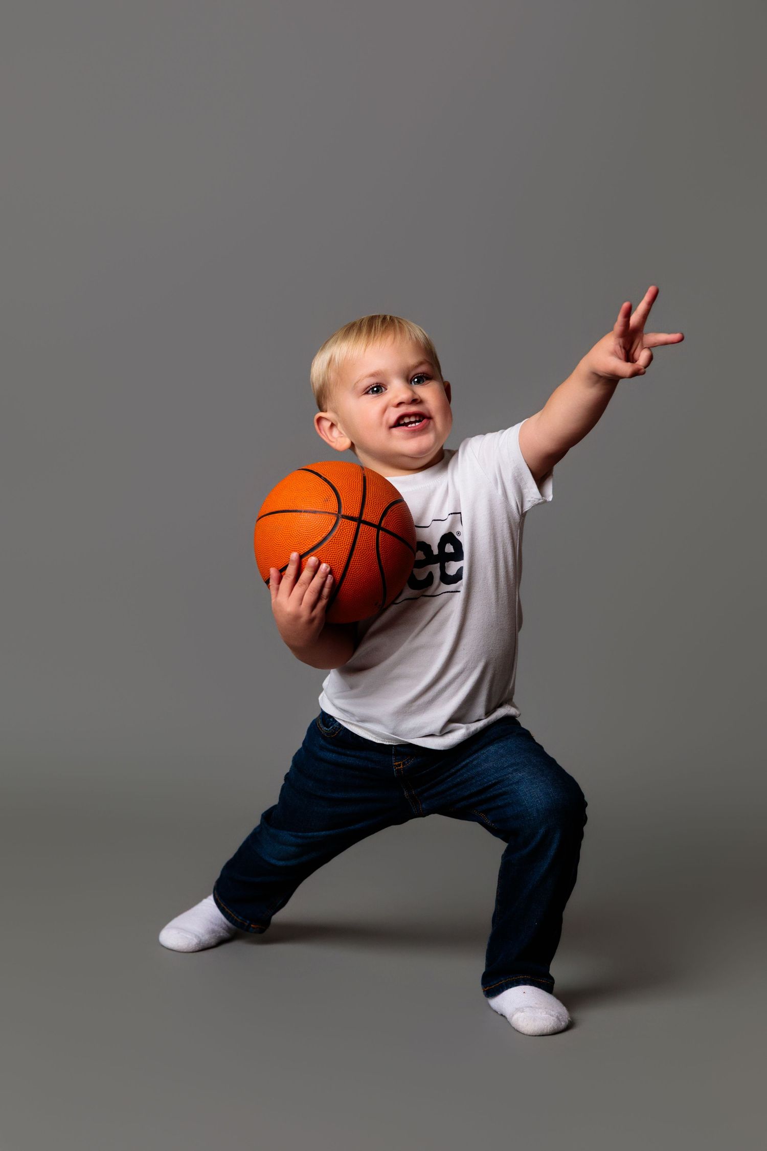 Energetic child in white shirt playing with basketball in dynamic pose against studio background.