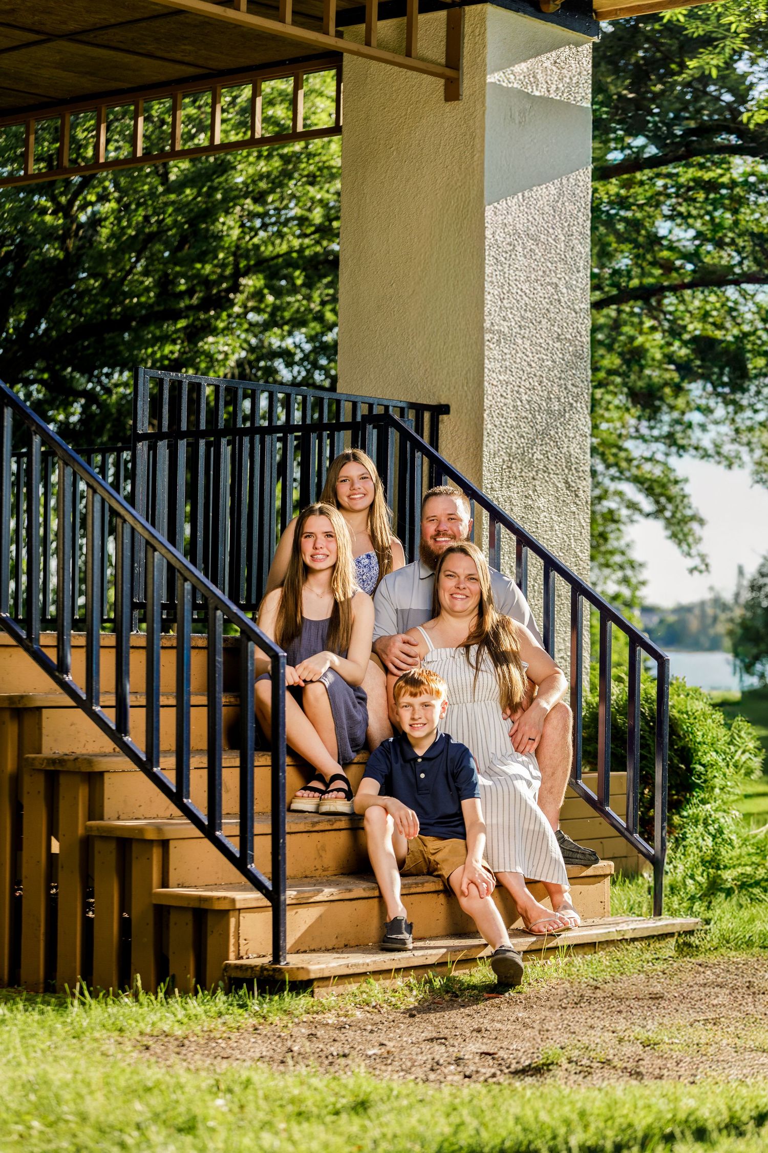 Family of five posing on outdoor stone steps beneath a covered structure with lake views.