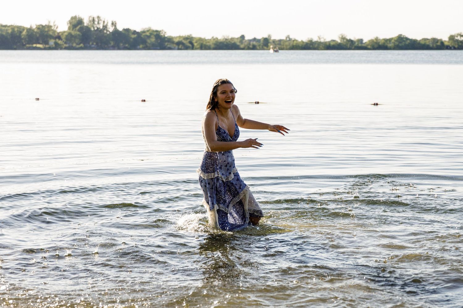 Woman in blue floral dress wading in a lake at golden hour with water splashing around her.