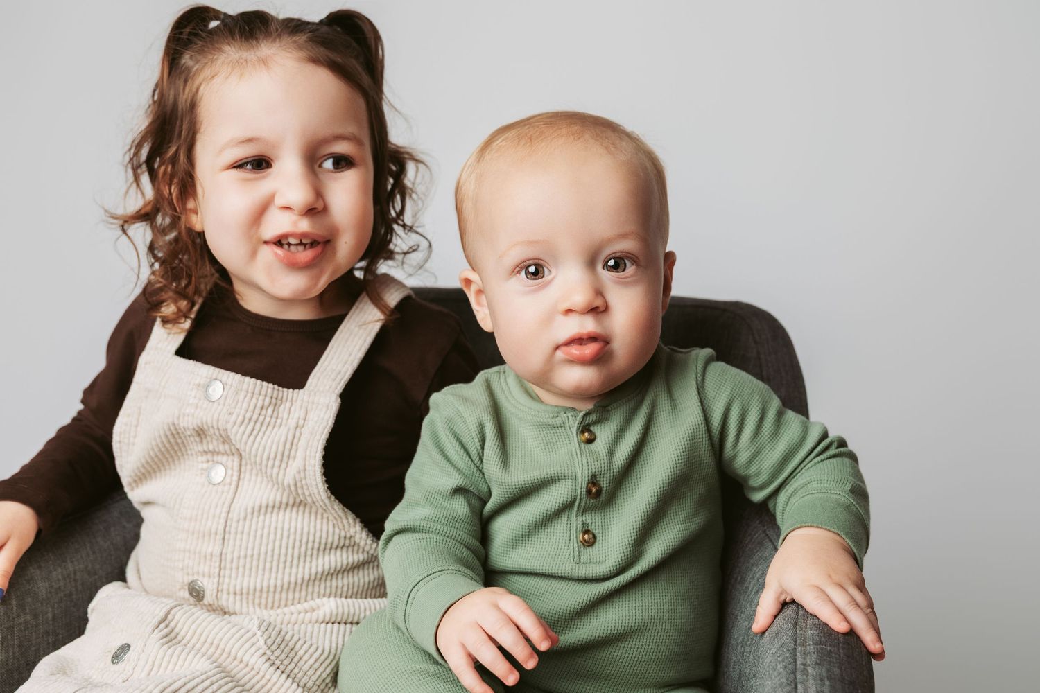 A family wearing coordinated cream and sage green outfits poses together against a gray background.