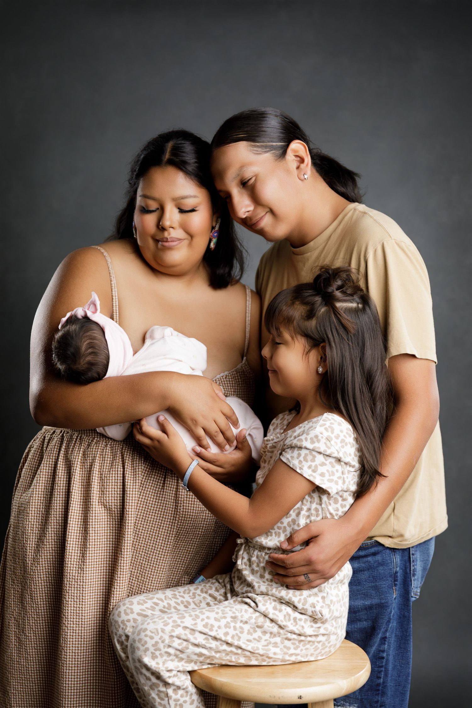 A family portrait of a mother holding a newborn baby, with a man and young girl gathered closely around her in a studio.