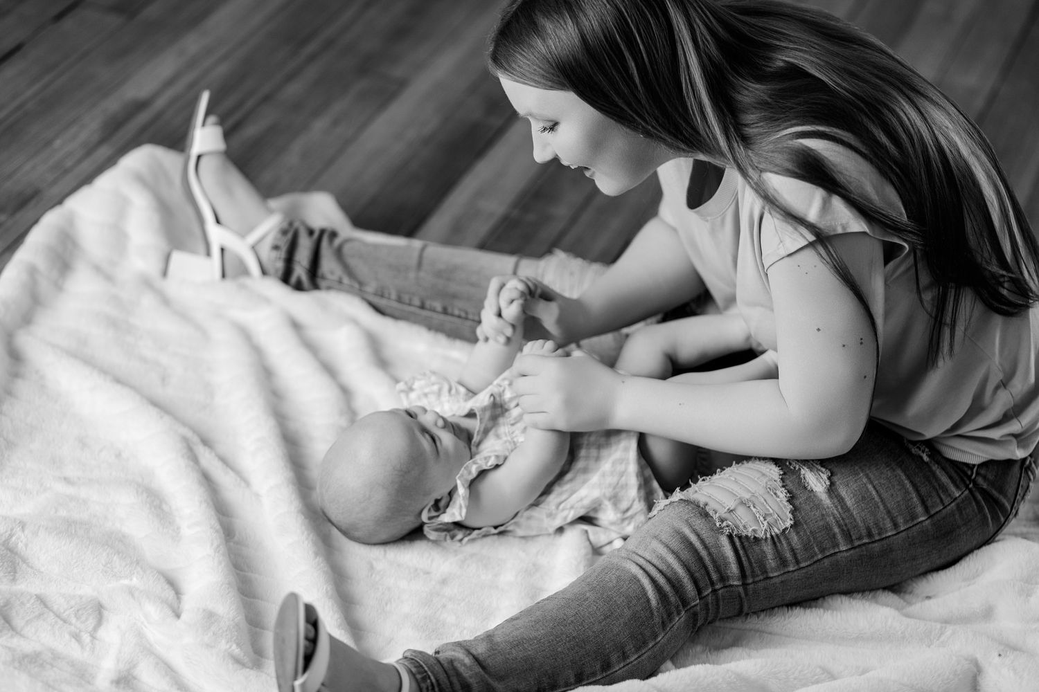 Black and white photo of young girl sitting on blanket playing with baby sibling on floor.