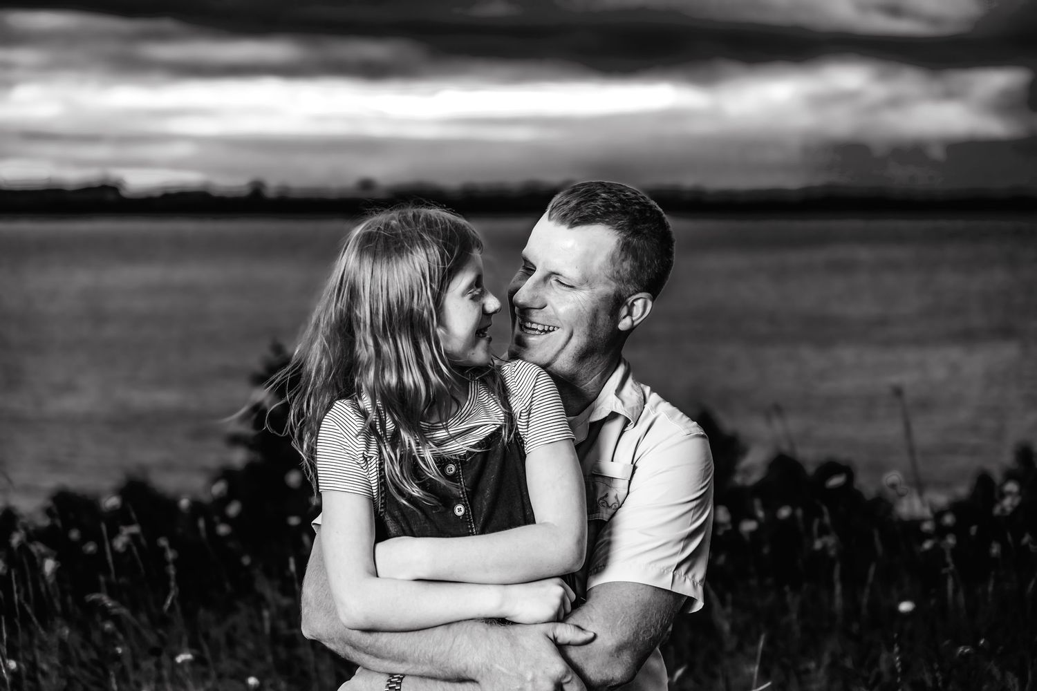 A romantic black and white photo series shows a couple embracing in a grassy field at sunset.