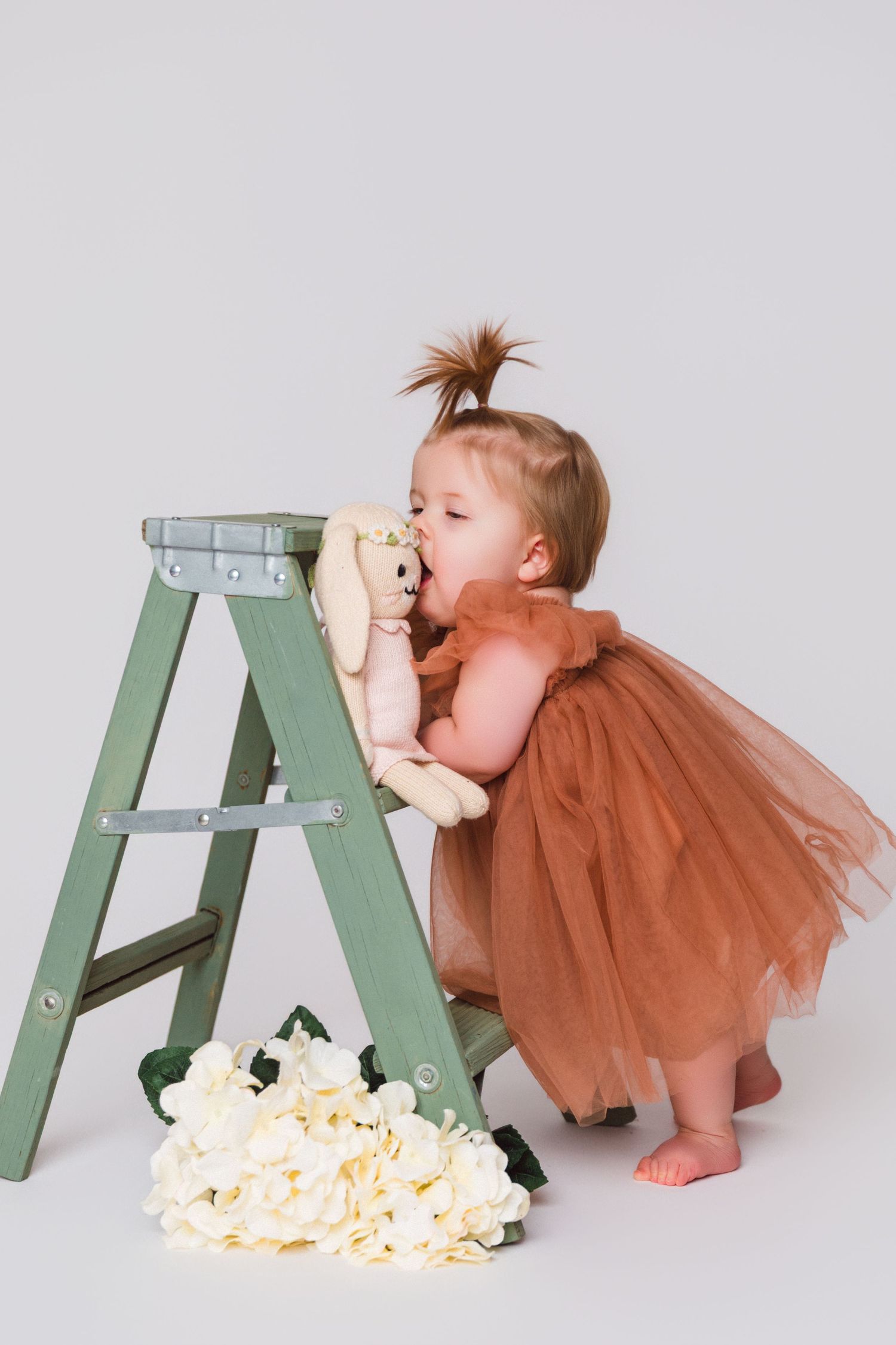Baby in a brown tulle dress eating popcorn next to a mint green ladder.
