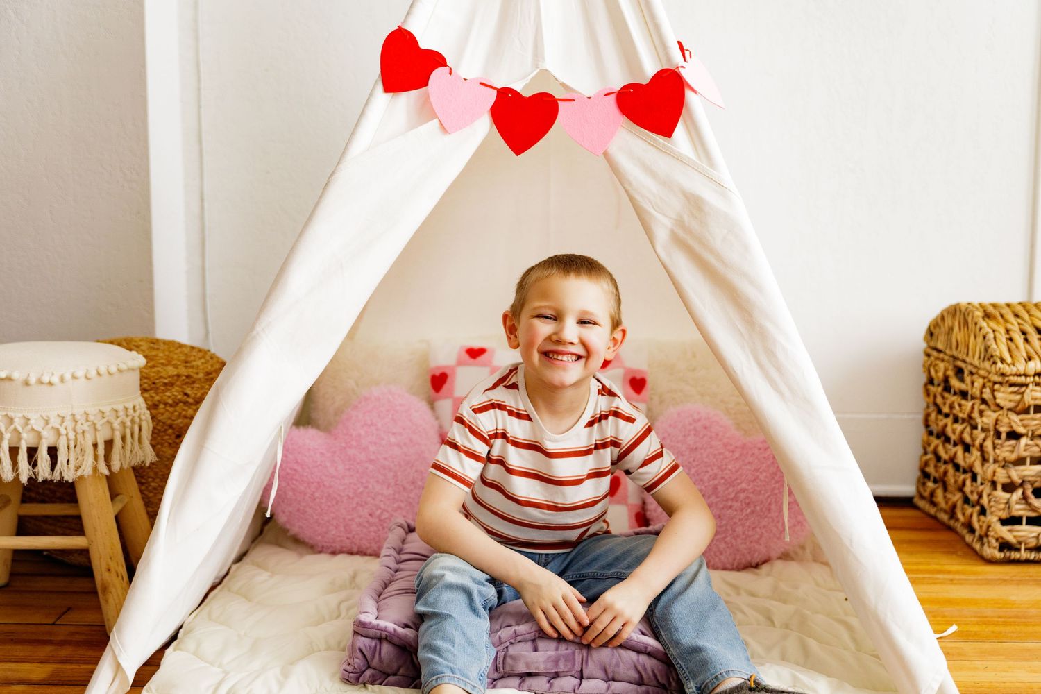 Cozy white teepee setup with pink cushions and red heart decorations for Valentine's day.
