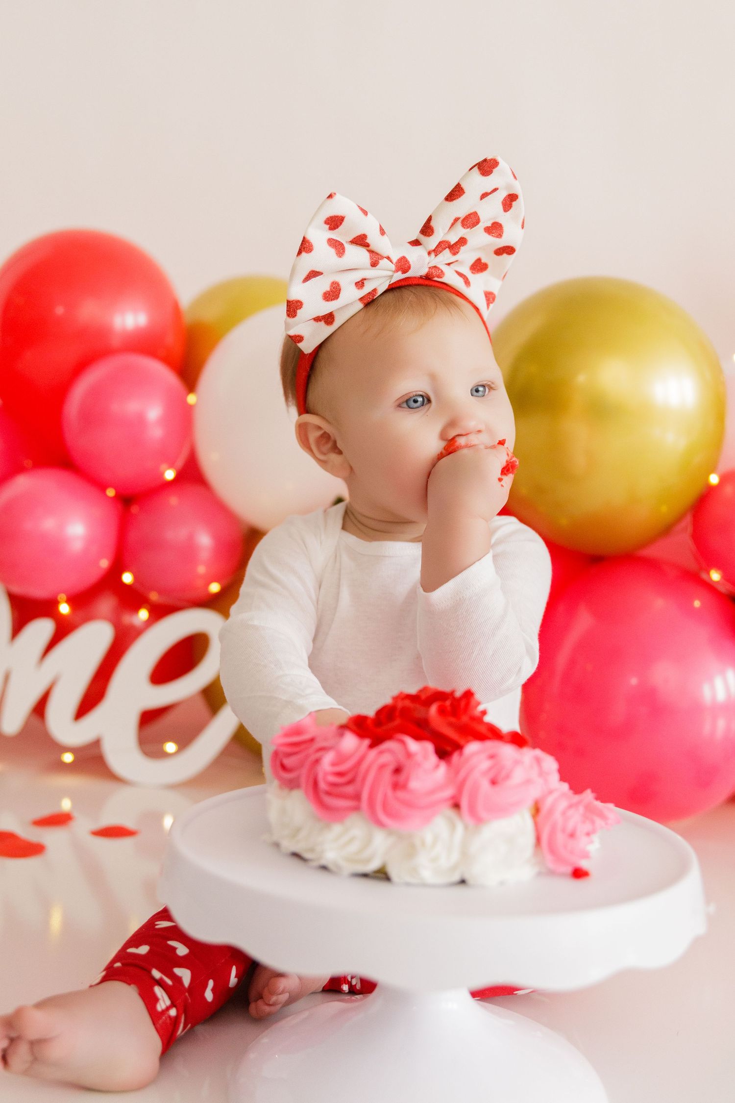 First birthday celebration setup with white cake stand and pink and gold balloon decorations.