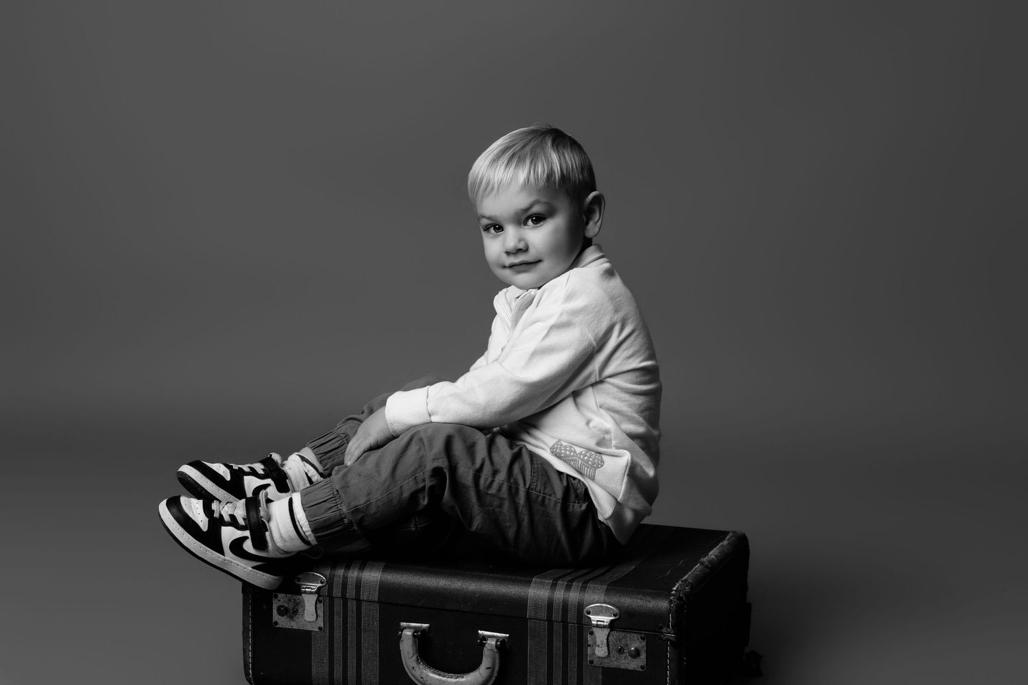 A child reclines on a dark leather chair in a studio portrait setting.