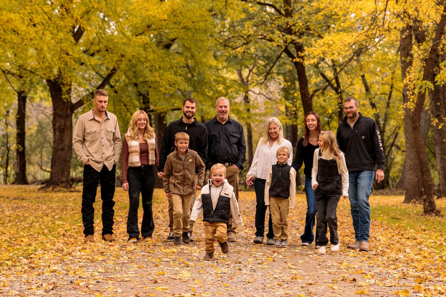 Group of people walking through a park with golden fall foliage.