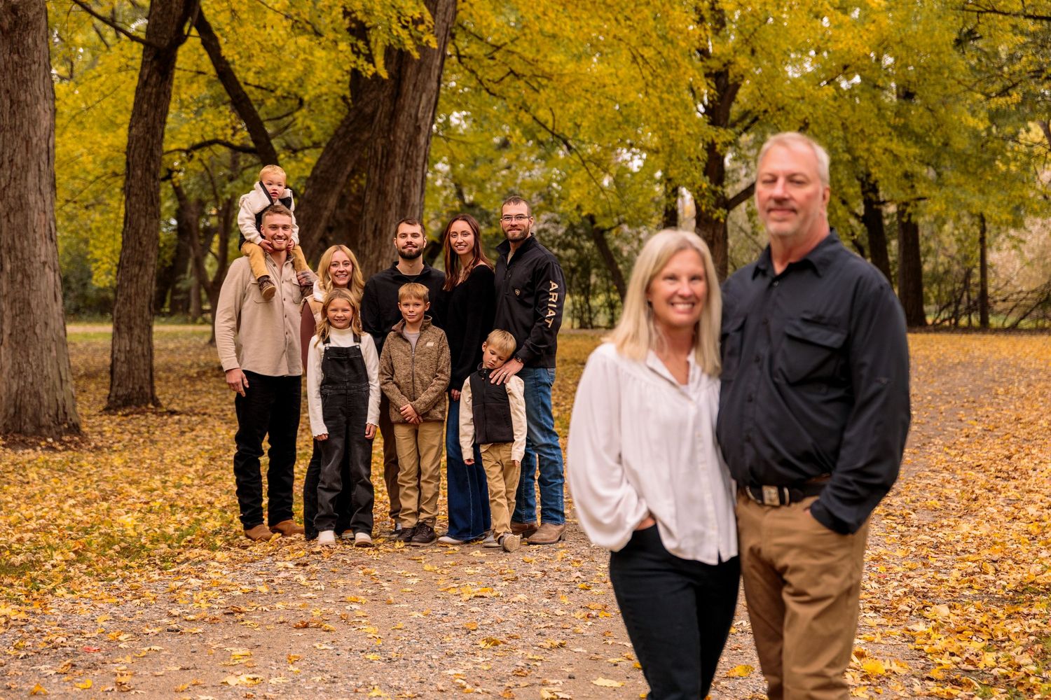 Extended family walking together on leaf-covered path during autumn photo session.