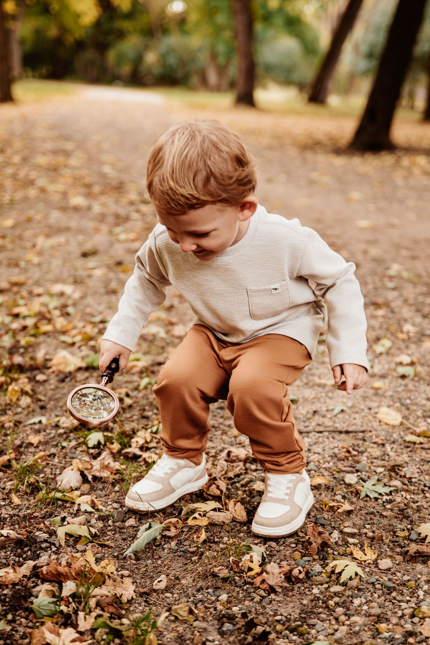 Close-up shots of a child exploring and touching autumn leaves on the ground while wearing white sneakers and brown pants.