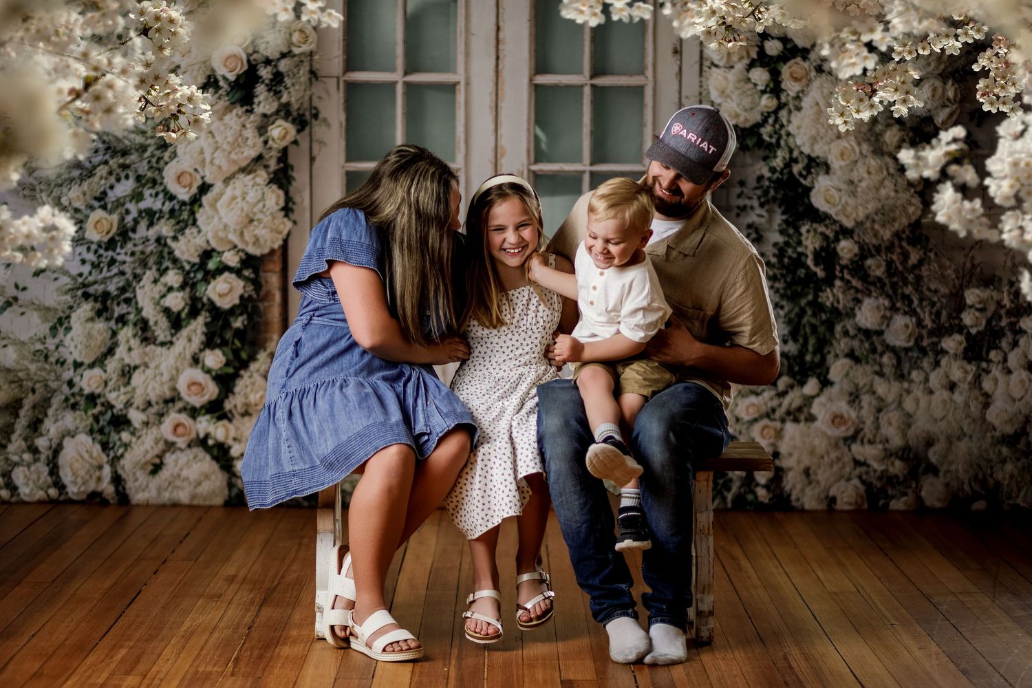 Family of four posing together with white floral backdrop in a warm studio portrait session.