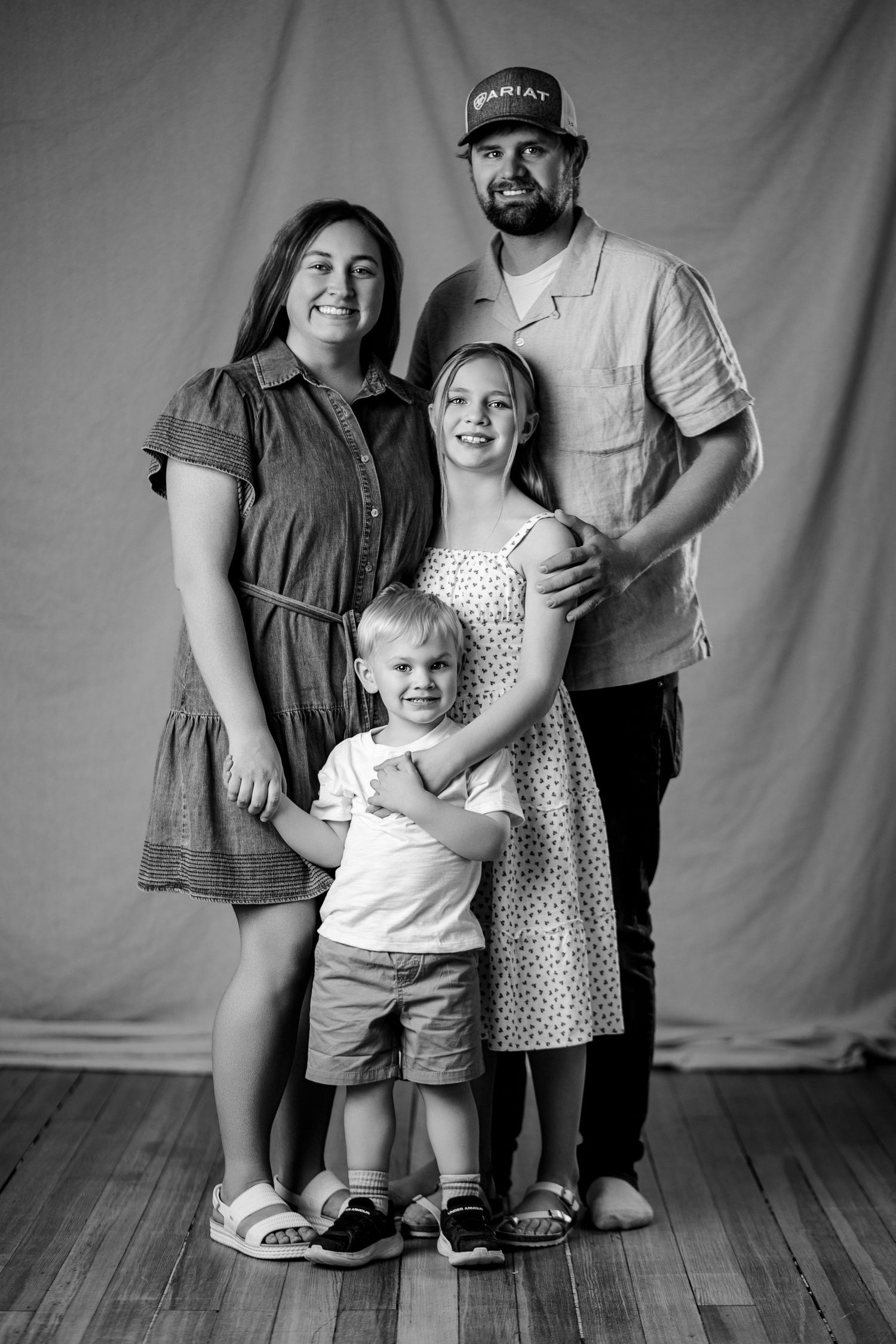 Black and white family portrait of two parents with a young girl and toddler boy posing together against a draped backdrop.