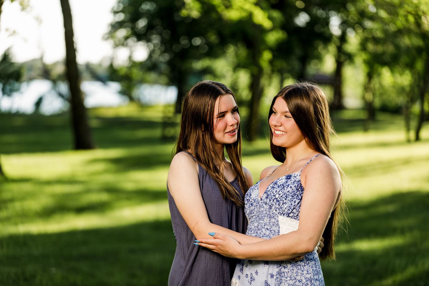 Two young women embracing and smiling at each other in a sunny green park.