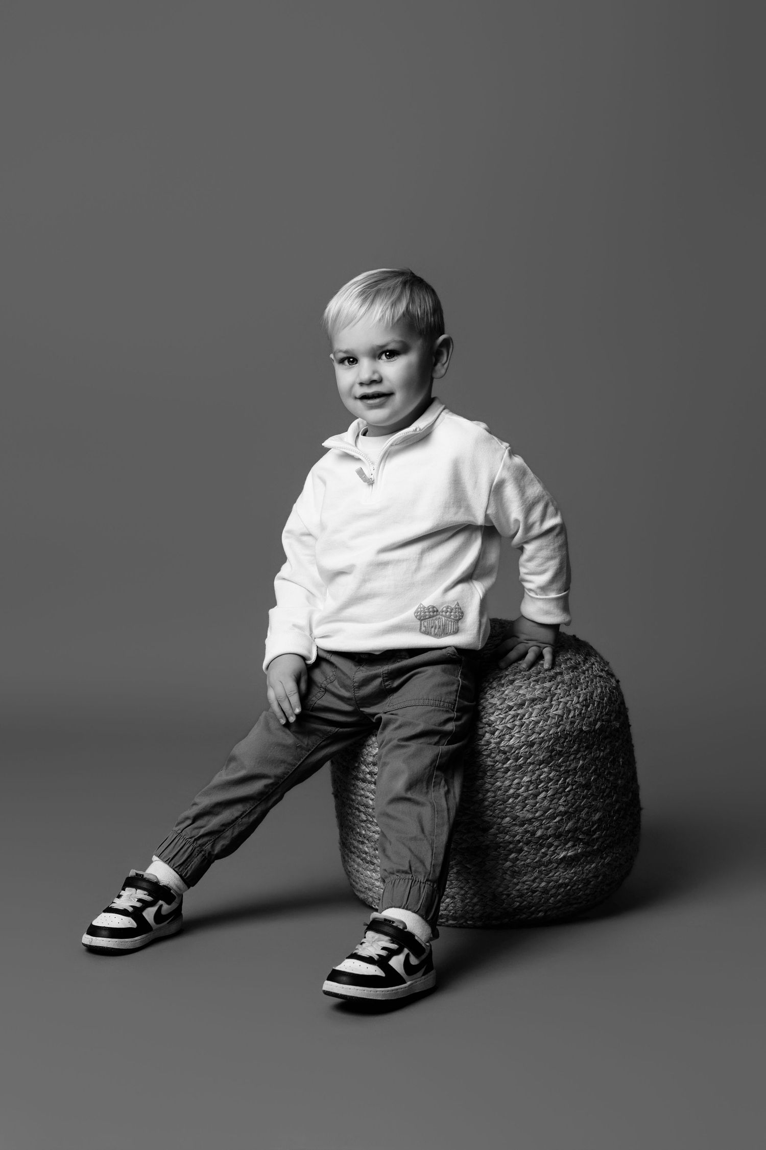 Black and white studio portraits of a young child sitting on a textured prop against a dark background.