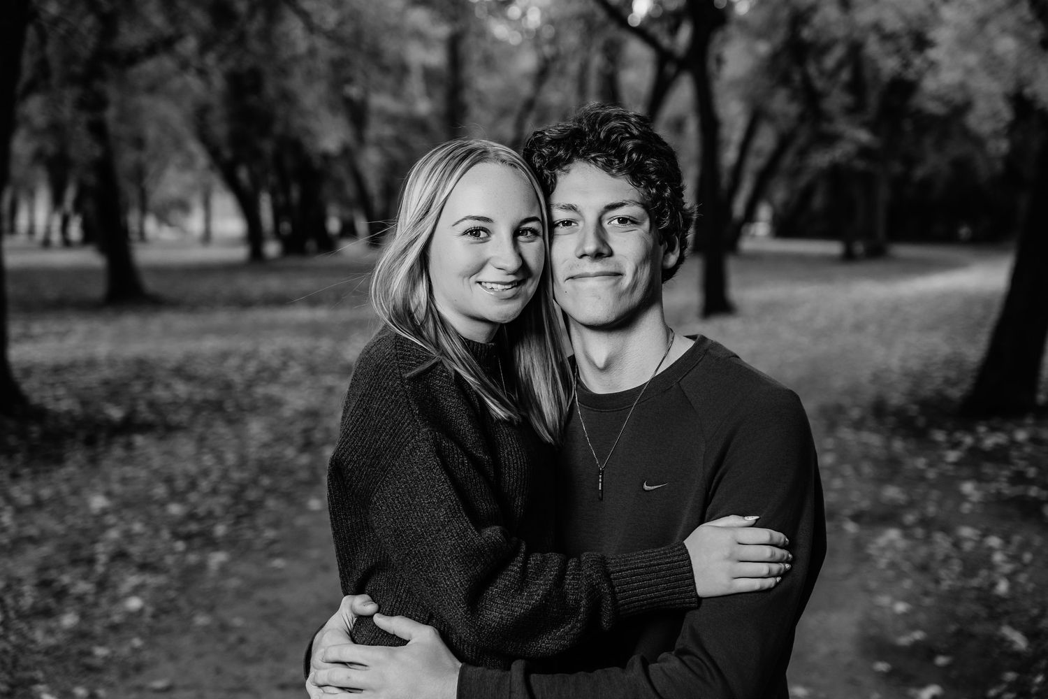 A black and white photo of people embracing outdoors with trees in the background.