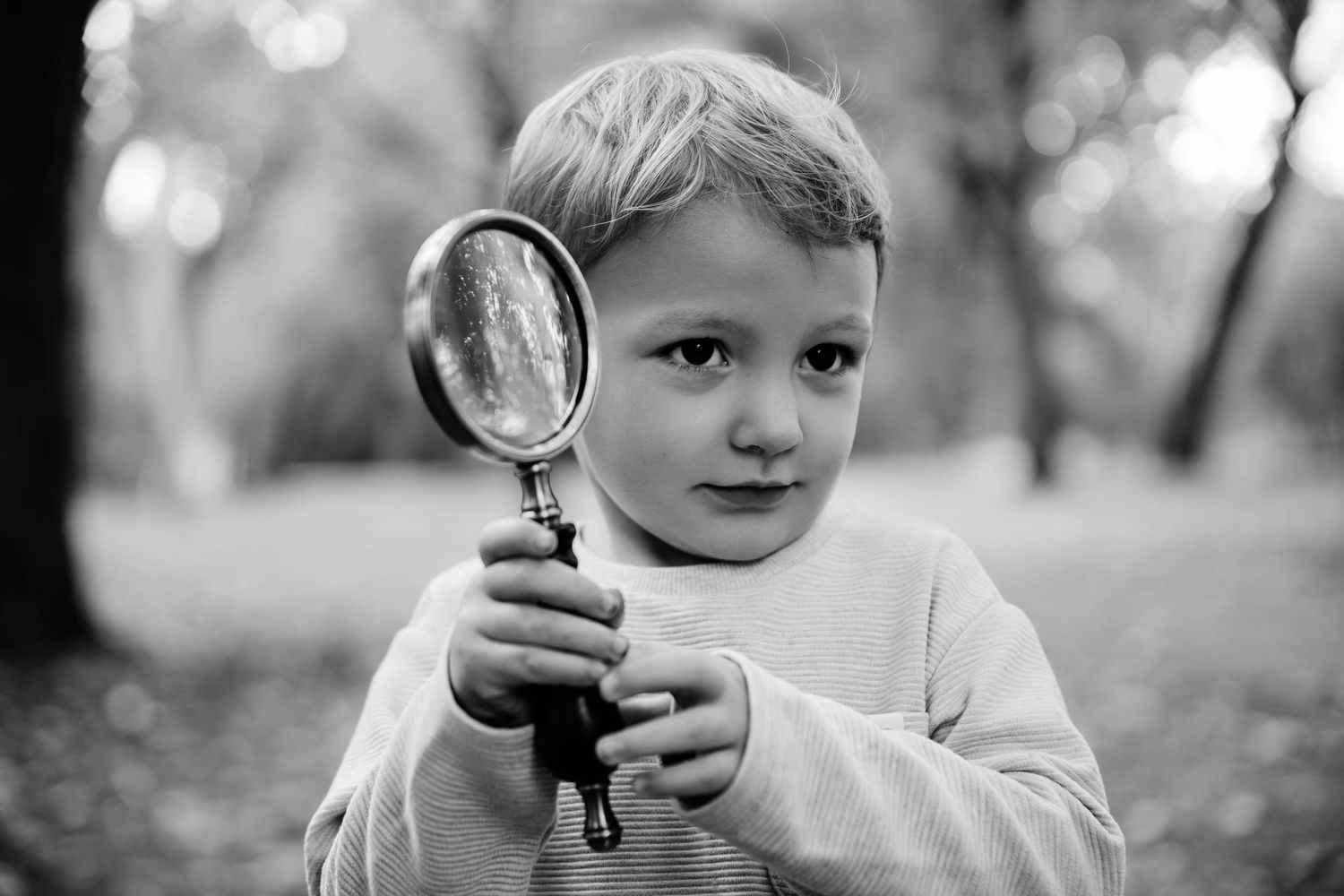 Child exploring with magnifying glass during outdoor family photoshoot.