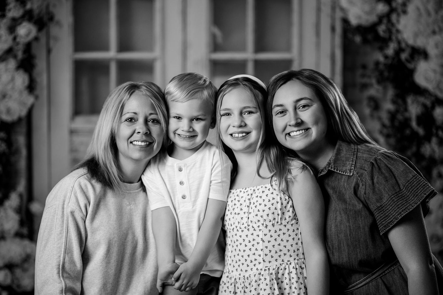 Black and white family portrait of mother with two daughters and young son smiling together.