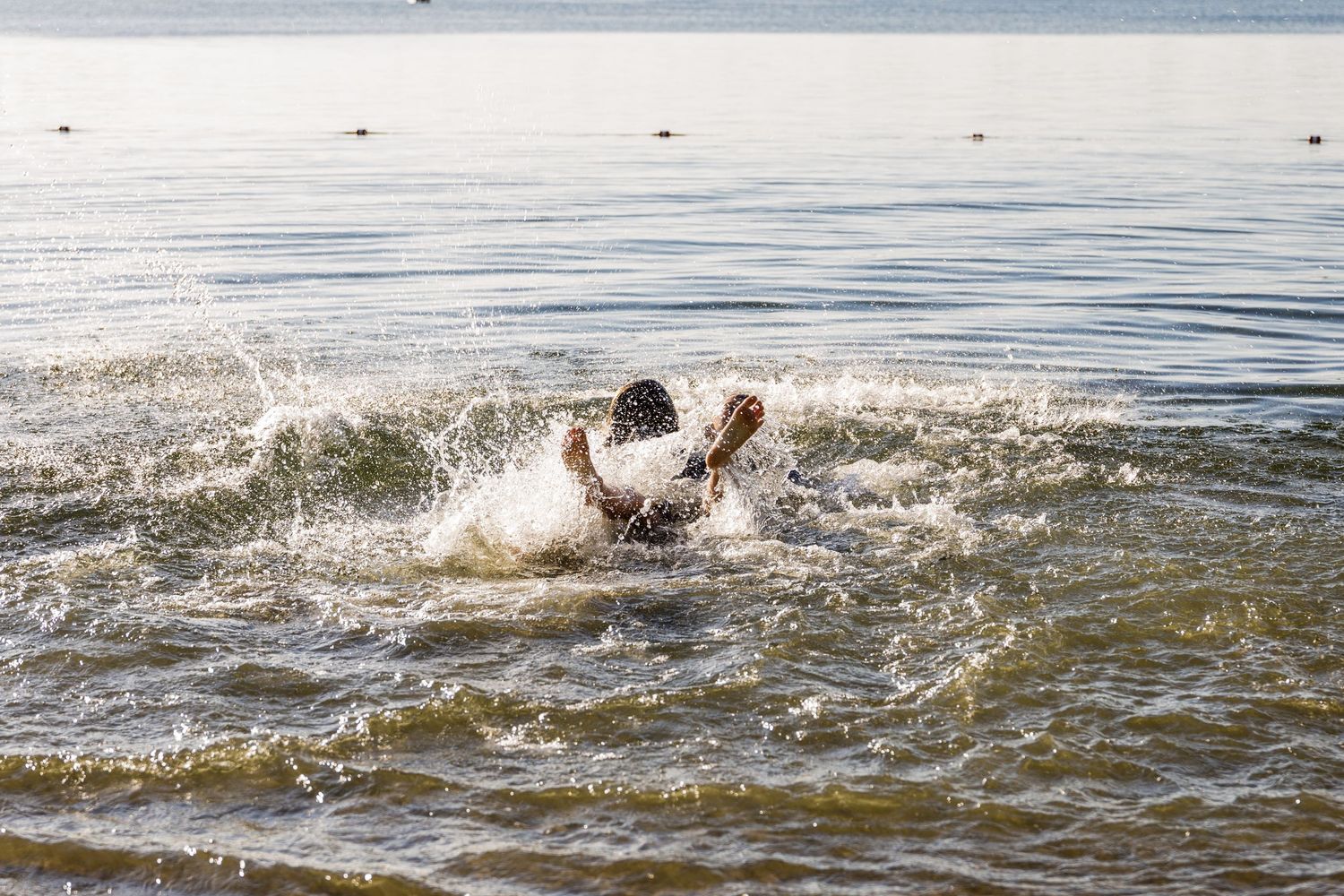 Person splashing dramatically in shallow lake water during a playful outdoor family photo session.