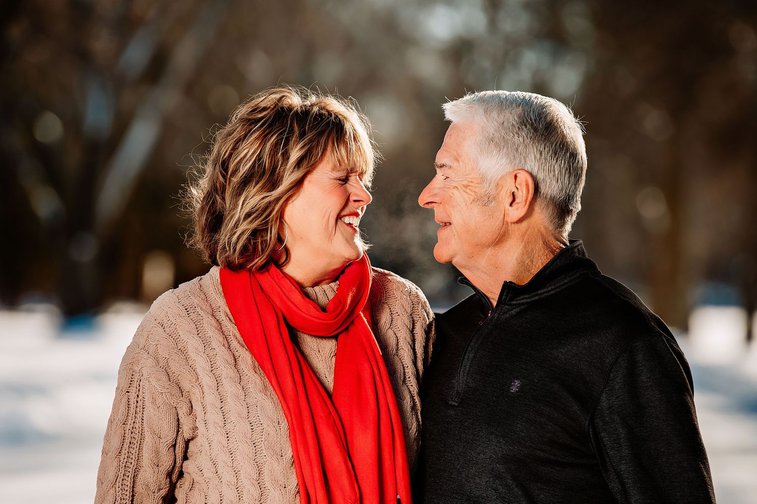 A couple shares a joyful moment together outdoors on a snowy winter day, with one wearing a bright red scarf.