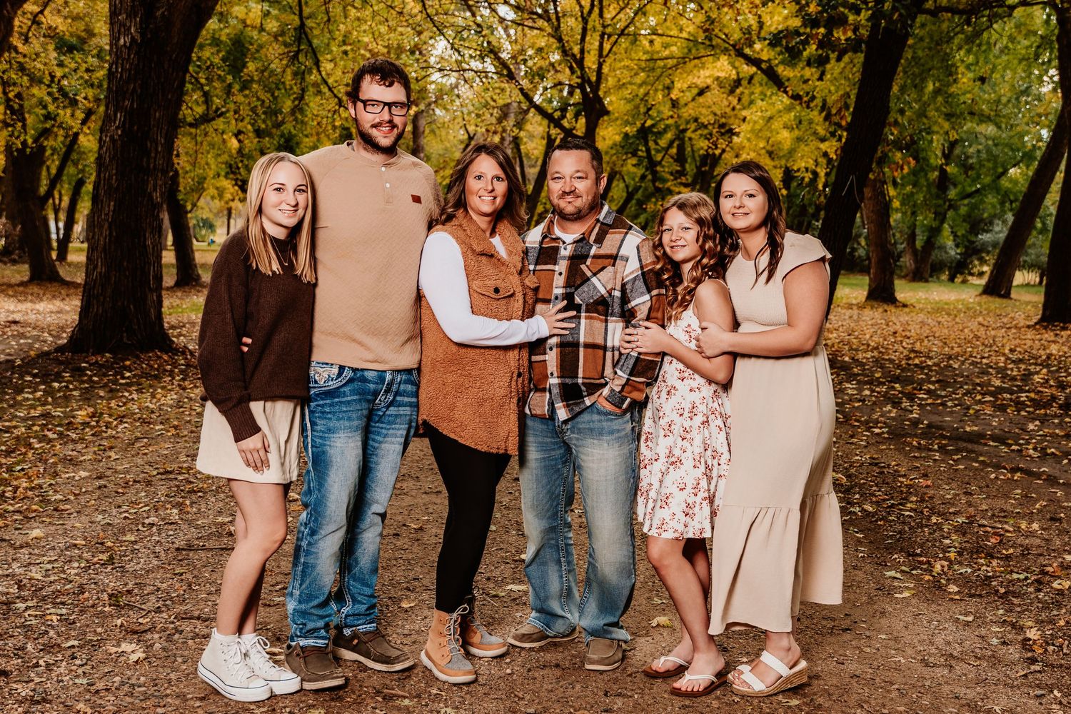 A group poses together in a wooded autumn setting with fallen leaves on the ground during a photo session.