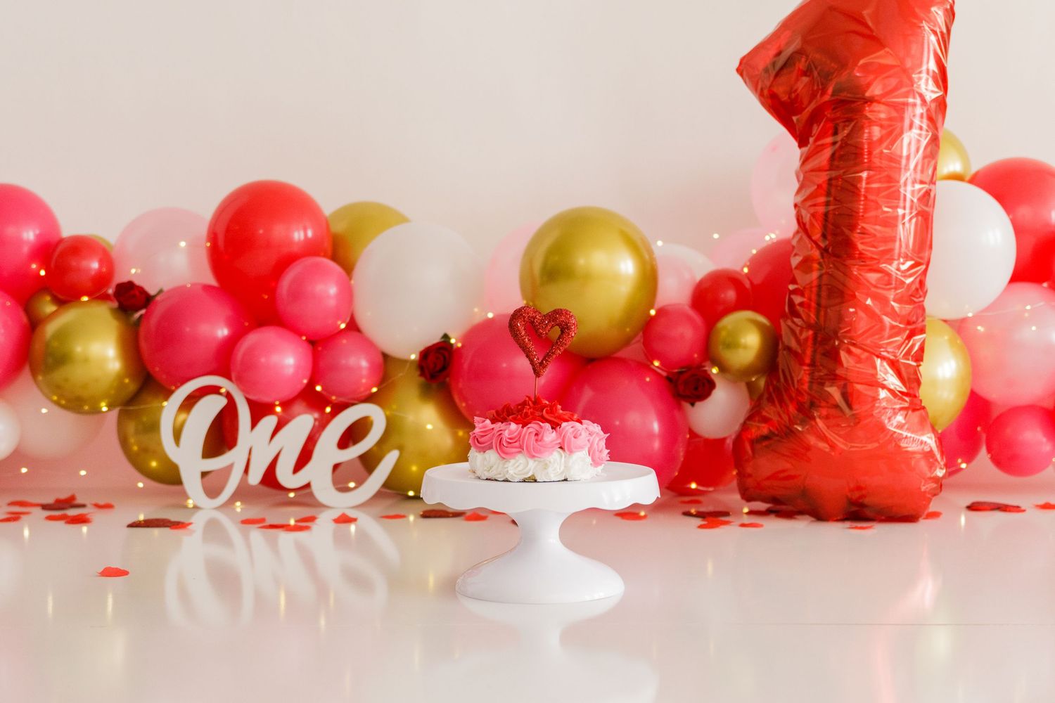 Red balloon garland with gold accents and 'One' sign for birthday celebration.