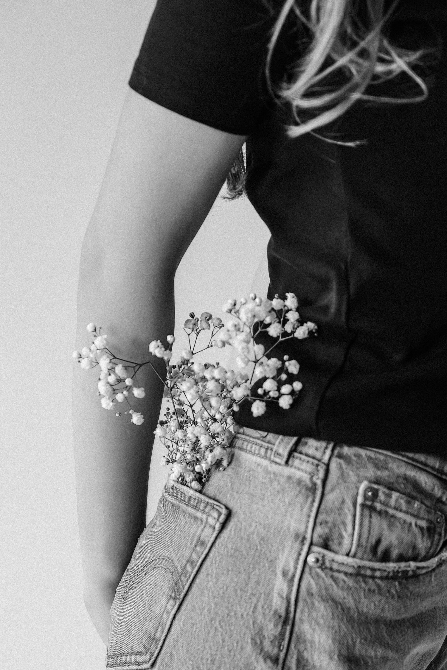 Close-up black and white photo of wildflowers tucked into denim jeans waistband.