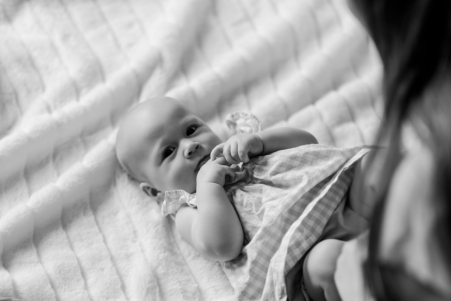 Black and white close-up of newborn baby lying on blanket holding a small toy pacifier.