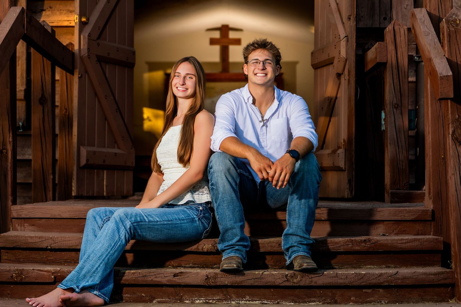 Couple in casual denim outfits sitting together on rustic wooden stairs in warm lighting.