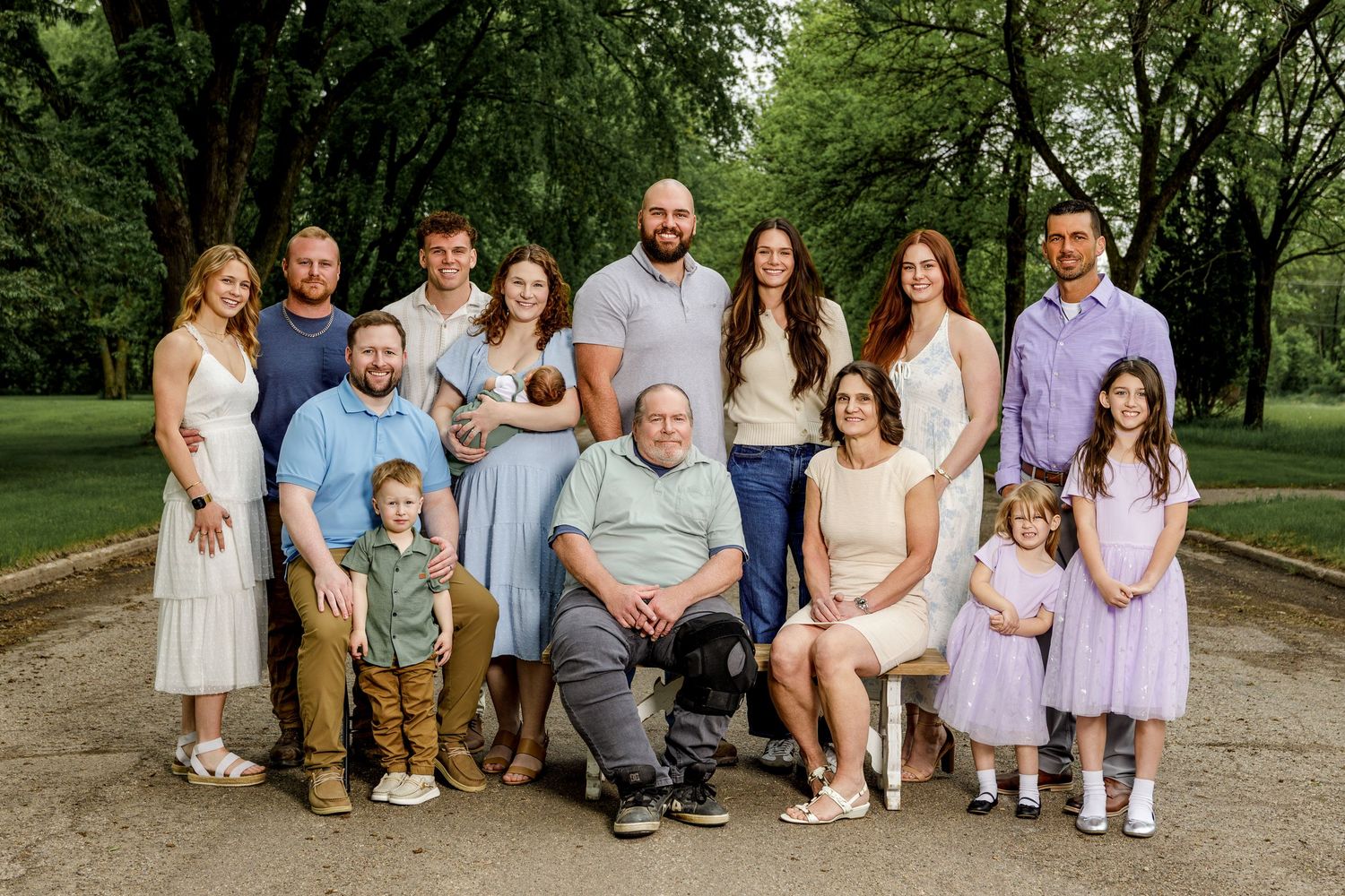 Large multigenerational family portrait outdoors in a lush green park, featuring adults and children smiling together.