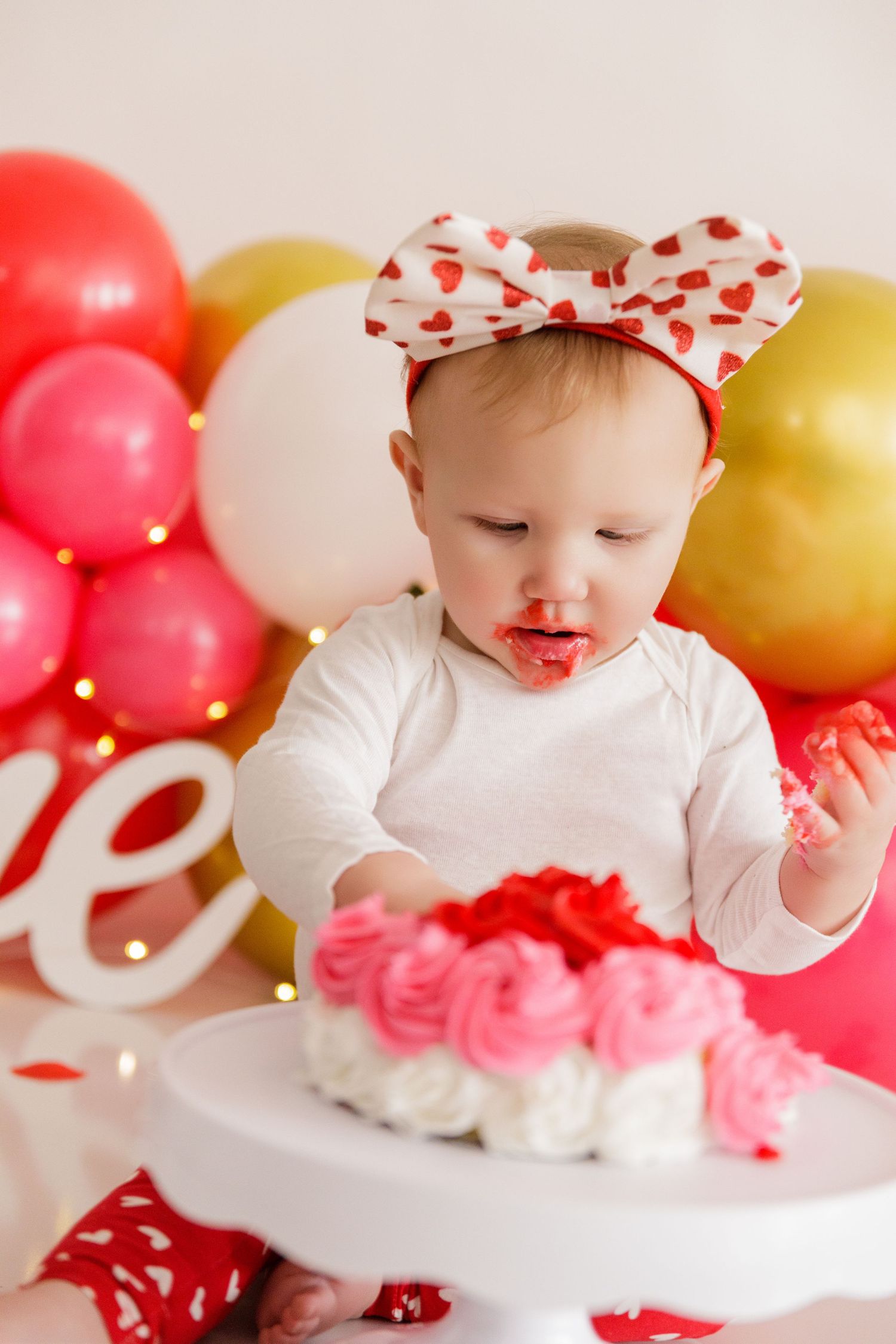 White cake stand decorated with pink frosting against a backdrop of festive balloons.