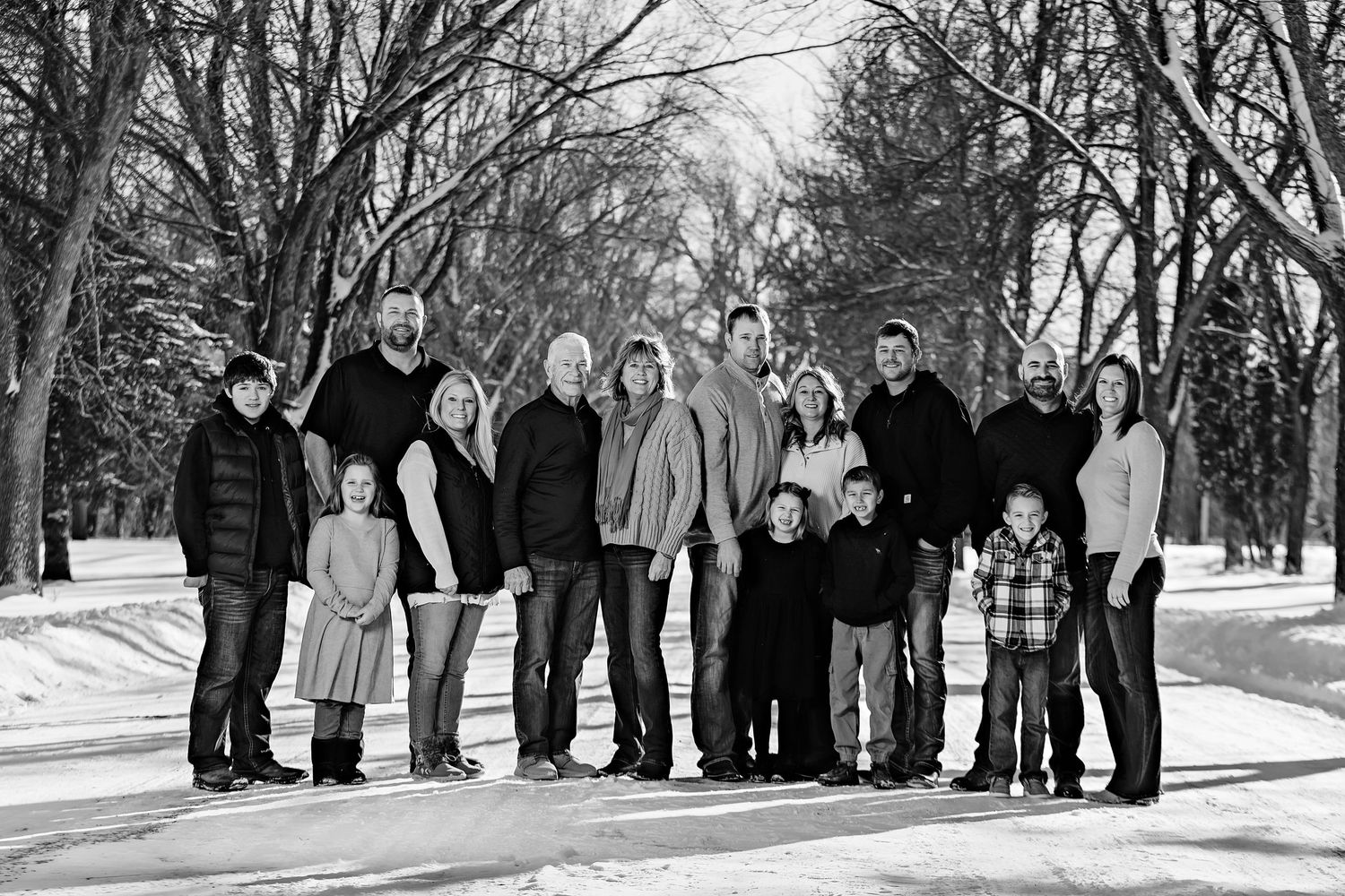 Multi-generational family standing together on a wintry path with snow and leafless trees in background.