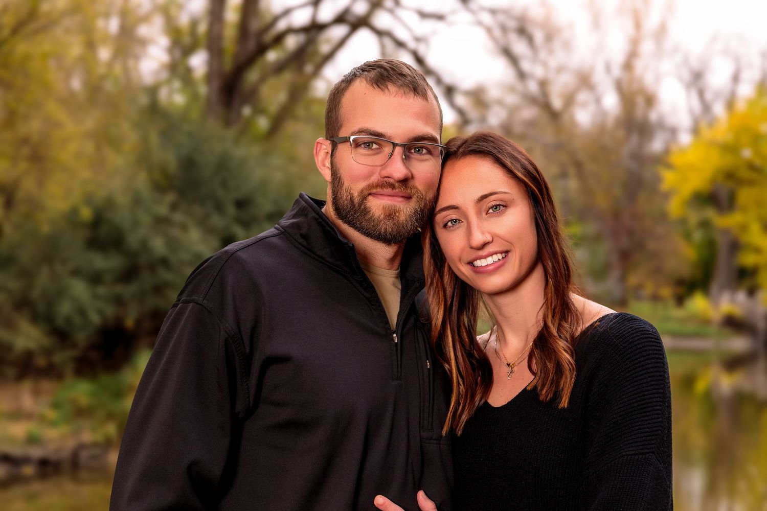Outdoor family photo session by a pond with autumn trees and natural lighting.