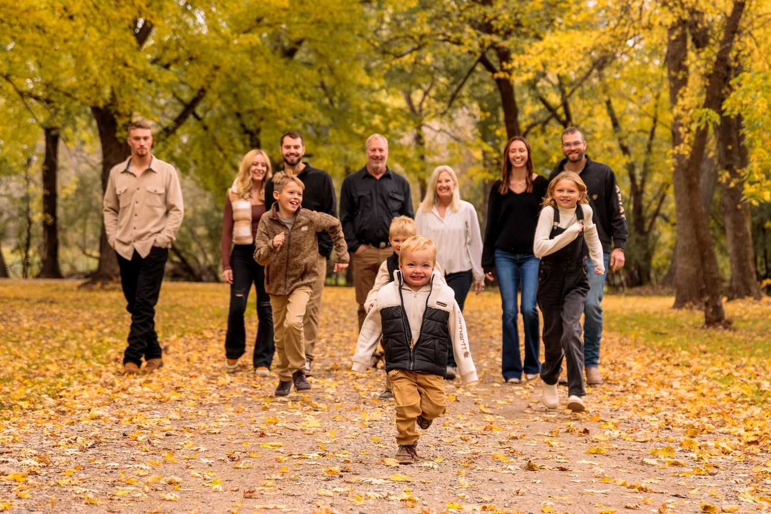 Group of people running and playing in a park filled with yellow autumn leaves.