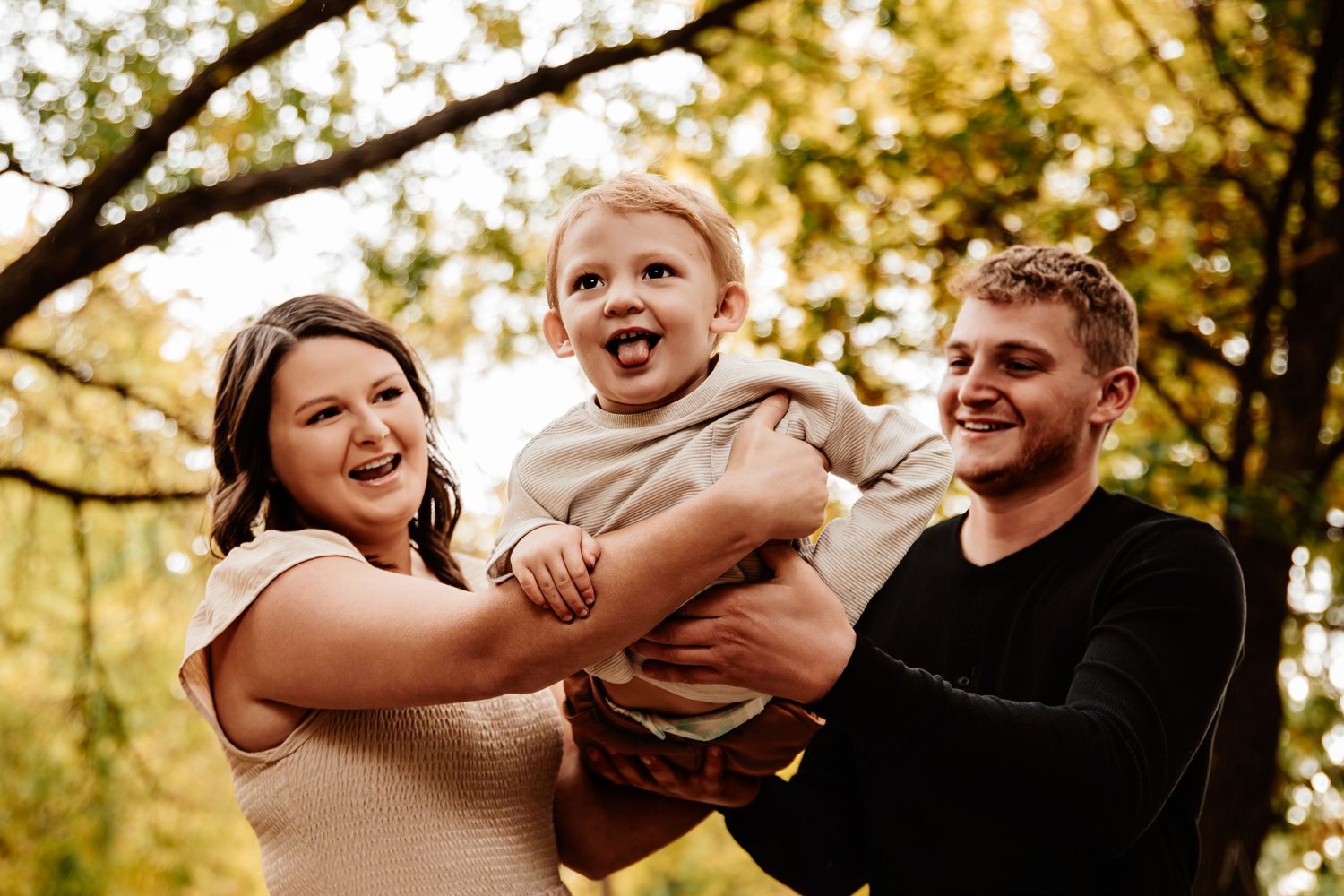 A family laughs together while posing for photos in an autumn forest setting.